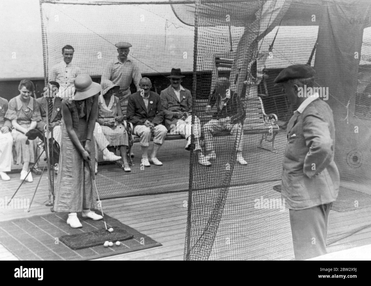 Deck games on board an ocean liner in the 1930s. Here a female passenger is taking part in a golf contest. She is aiming to hit the ball at a target painted on the back netting (right). Stock Photo