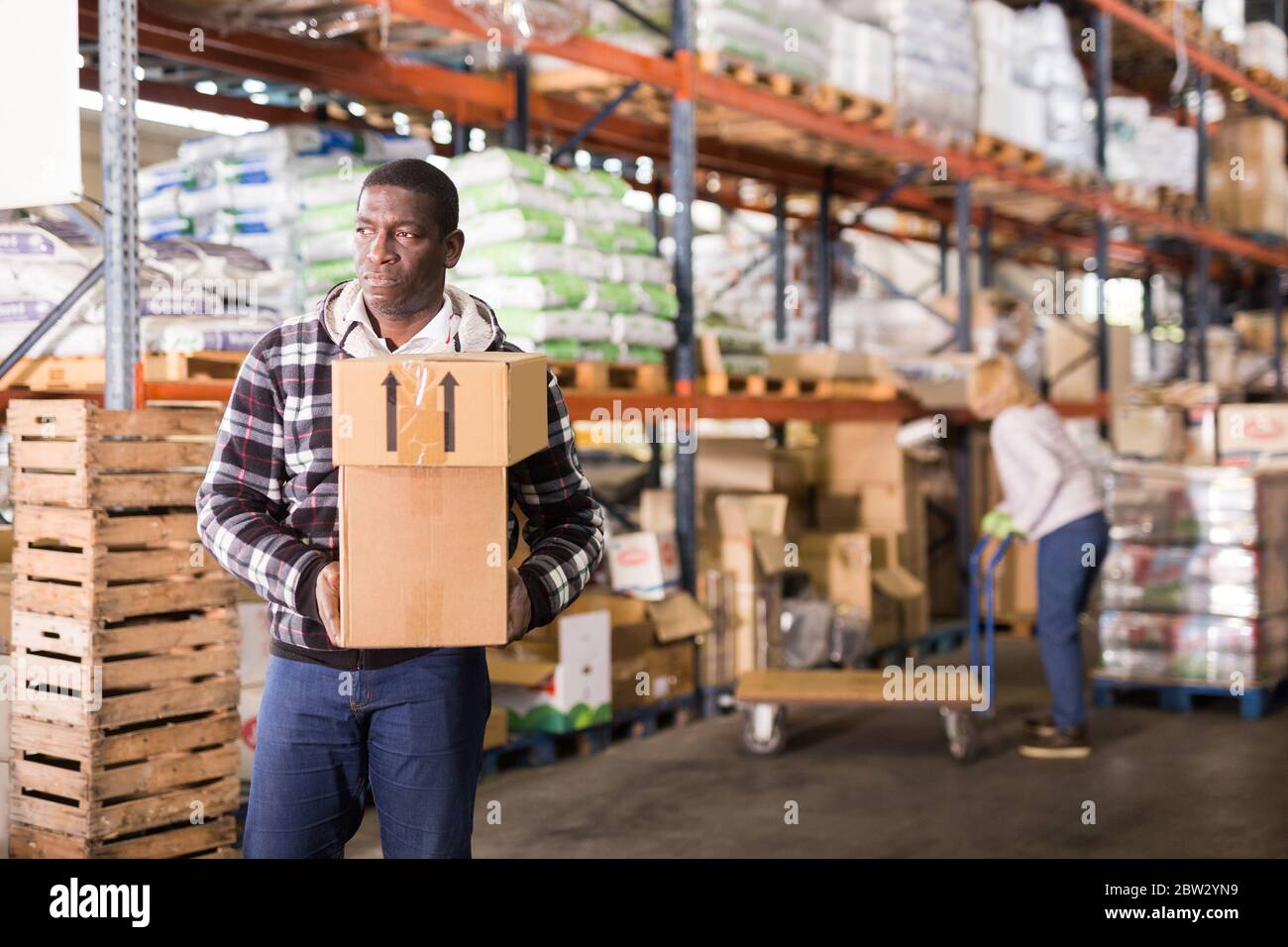 Focused african american man working in warehouse carrying cardboard ...
