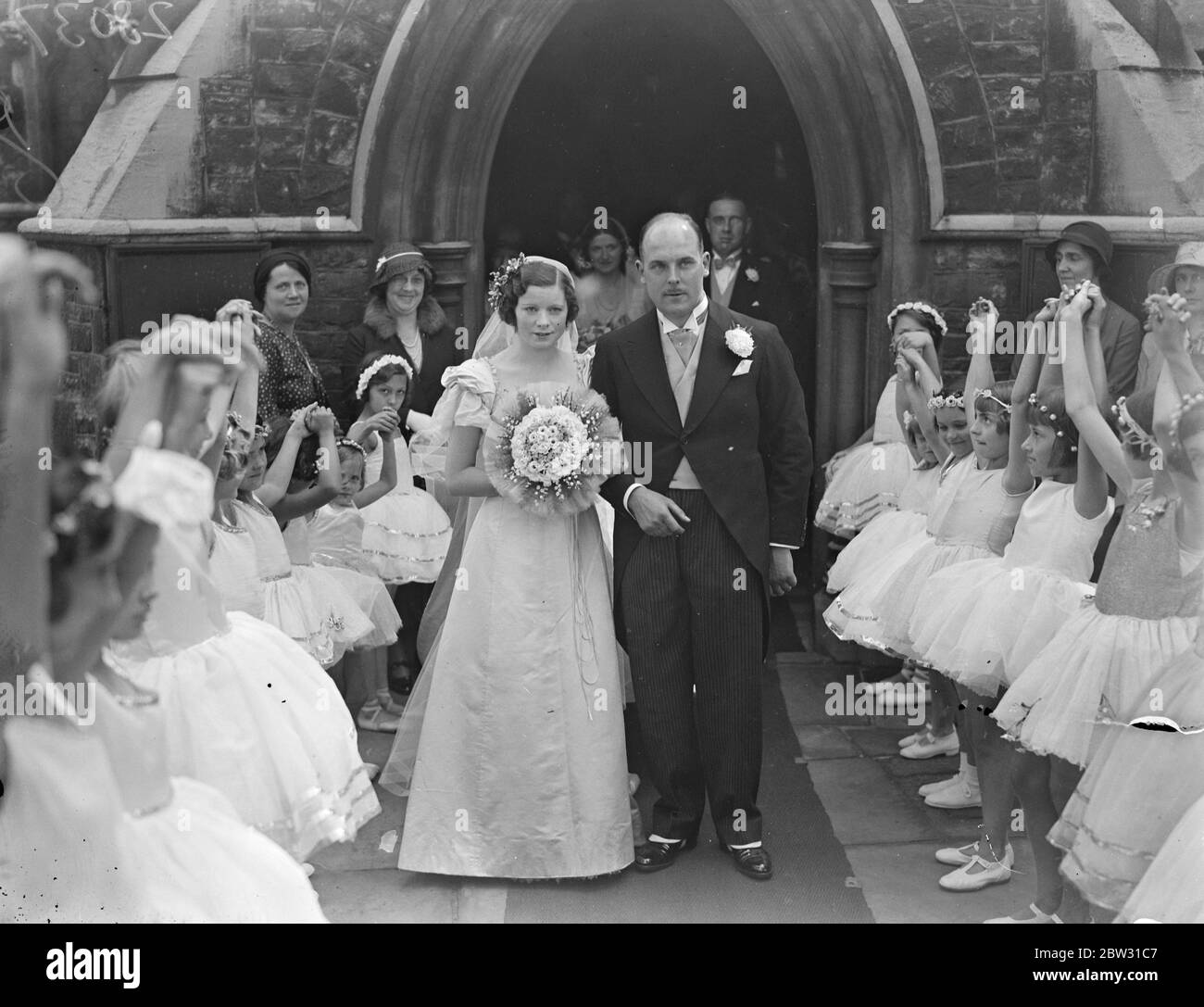 Bride 's guard of honour of ballet dancers . Champion ballroom dancer weds in thirty two year old wedding dress . Dressed in a wedding dress thirty two years old , which was worn by her bridesmaids mother at her wedding , Miss Gladys Fraser , the famous ballroom dancing champion was married at St Stephens Church , Gloucester Road , London , to Mr W E H Thomas of Manchester . The bride recently won the West of Scotland championship . The bride and groom leaving the church through a guard of honour of little ballet dancers . Miss Irene Ashton the ballet dancer , was chief bridesmaid . 31 August Stock Photo