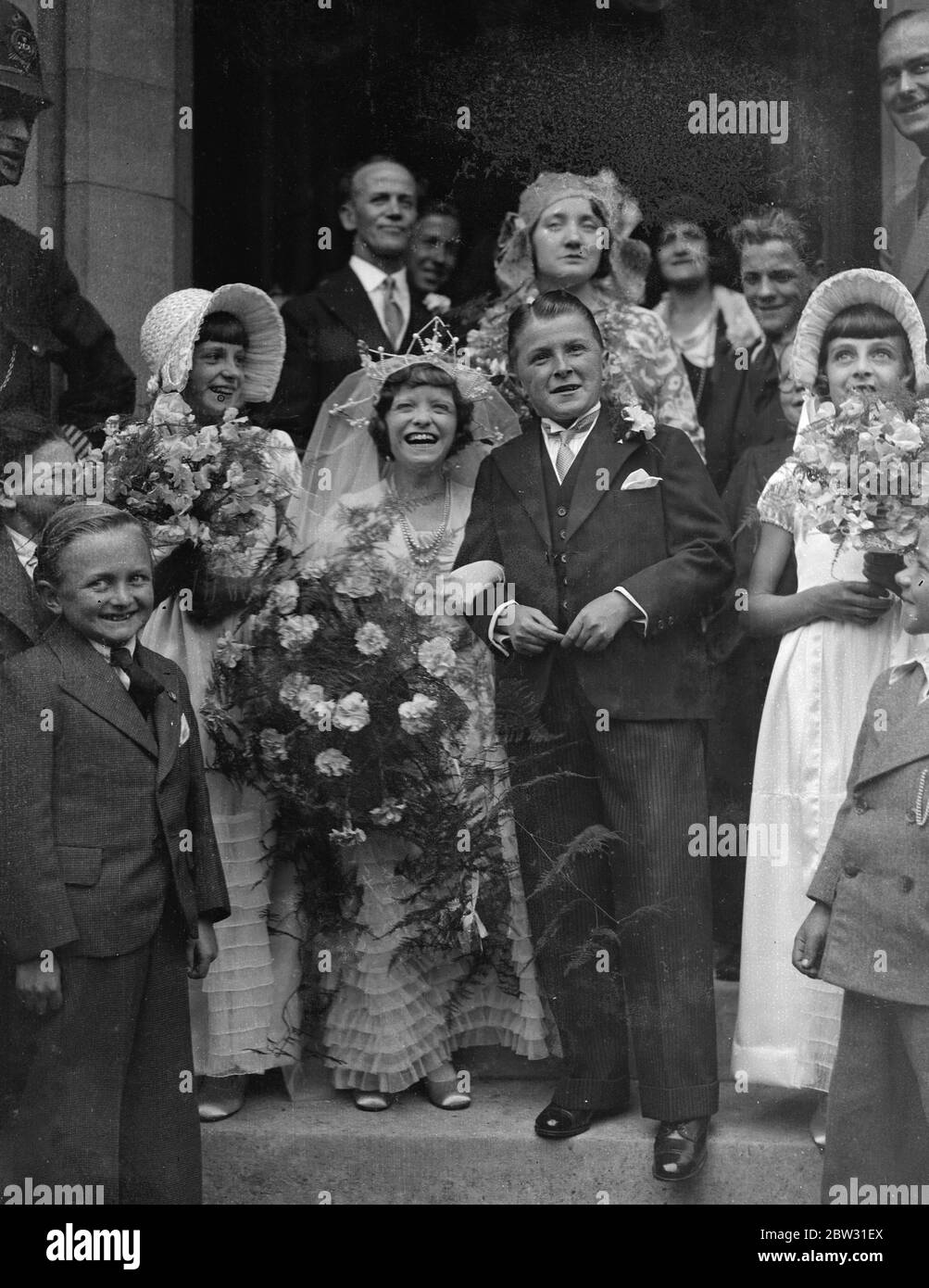 England ' s tiniest bride and groom marry at Mitcham . Miss Dorothy Kathleen Griffiths , who is only 3 feet 10 inches tall , and Mr Vivian Pascoe , who is two inches taller , both belonging to a midget circus troupe were married at St Barnabas Church , Mitcham , Surrey . The wedding was attended by members of the Theatrical Company with whom they are playing . The bride and groom with the bridal party at the wedding . 14 August 1932 Stock Photo