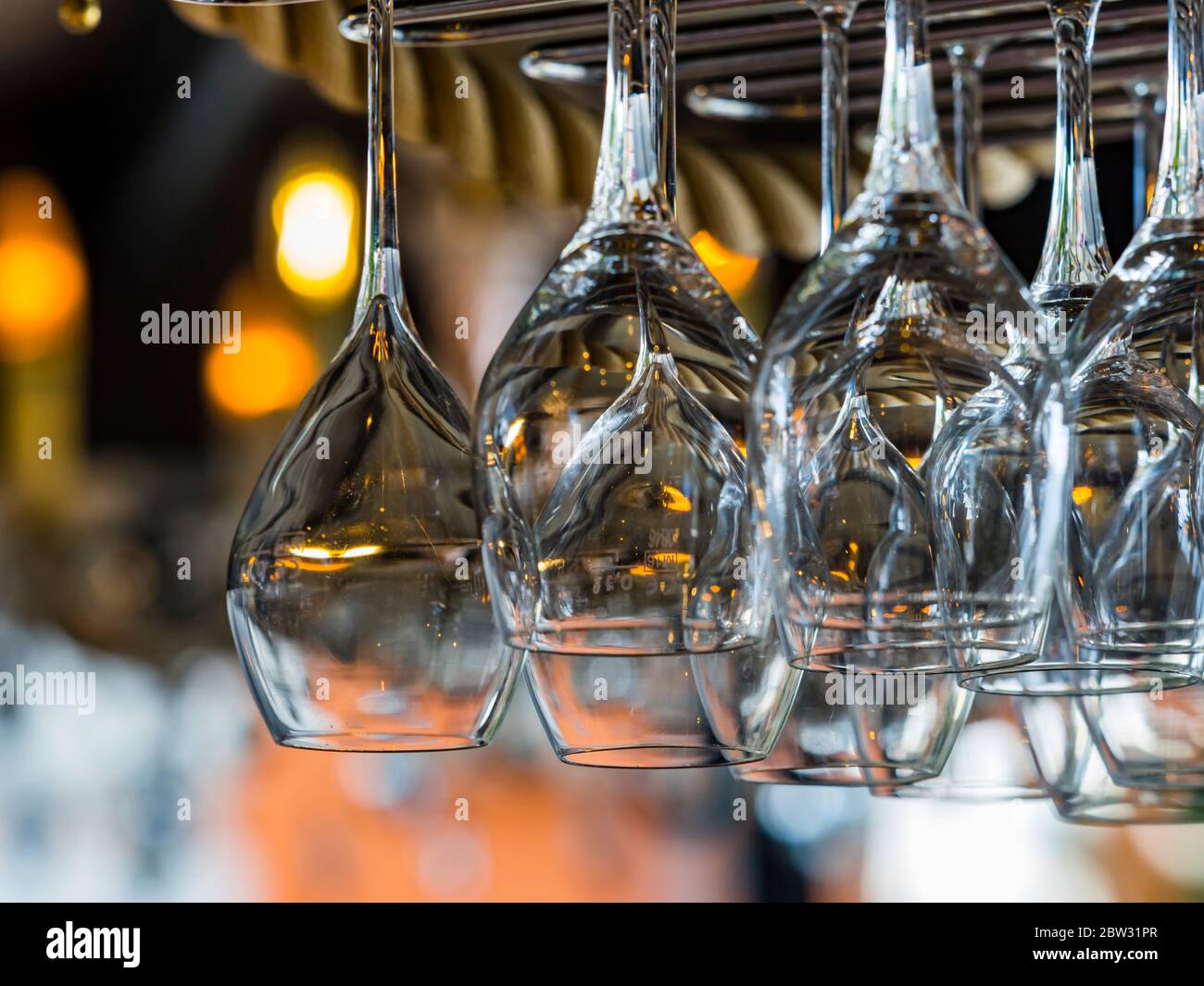 Many multiple bunch of drinking glasses empty ready clean washed cleaned hanging from above inverted in bar isolated Stock Photo
