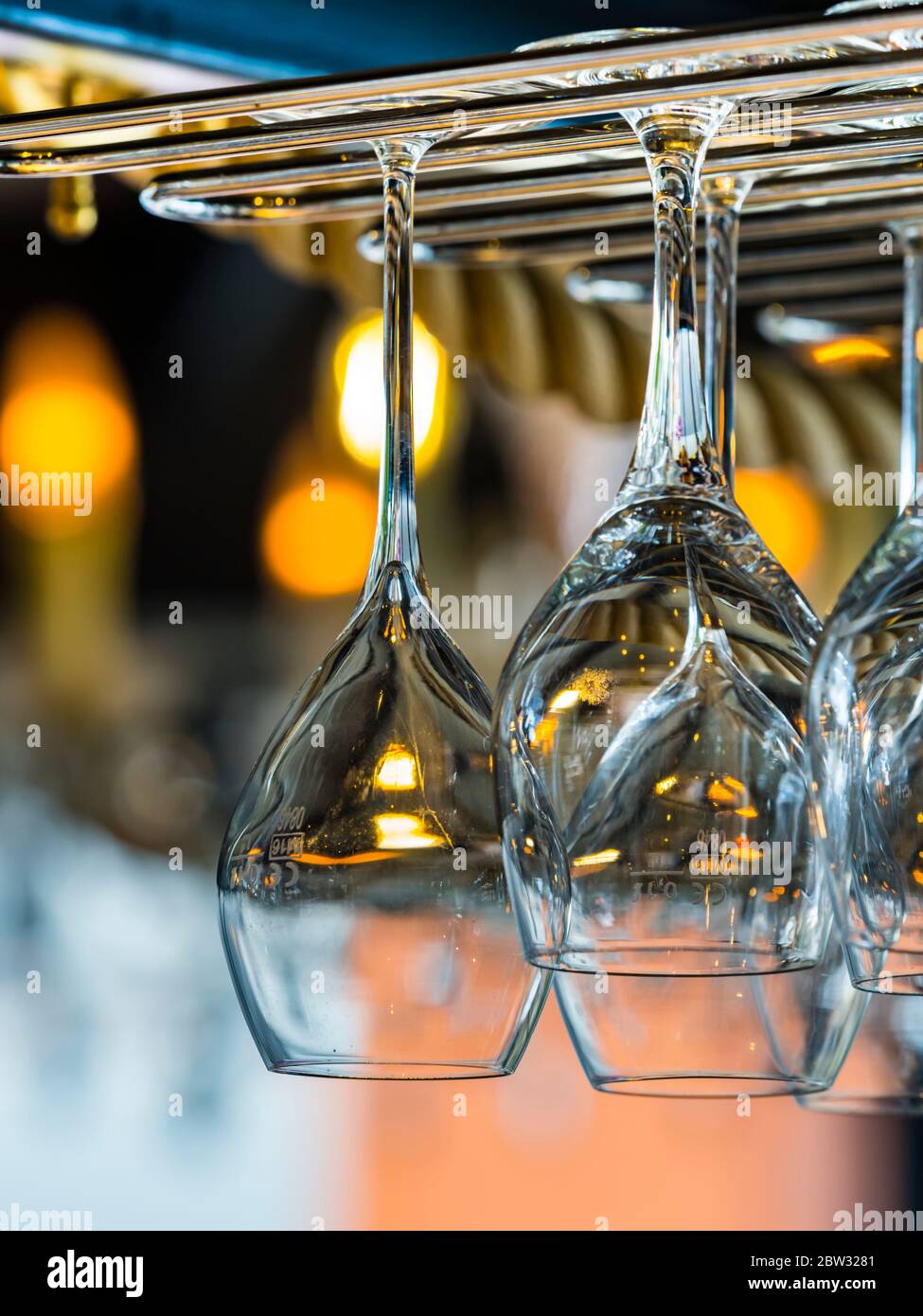 Many multiple bunch of drinking glasses empty ready clean washed cleaned hanging from above inverted in bar isolated Stock Photo