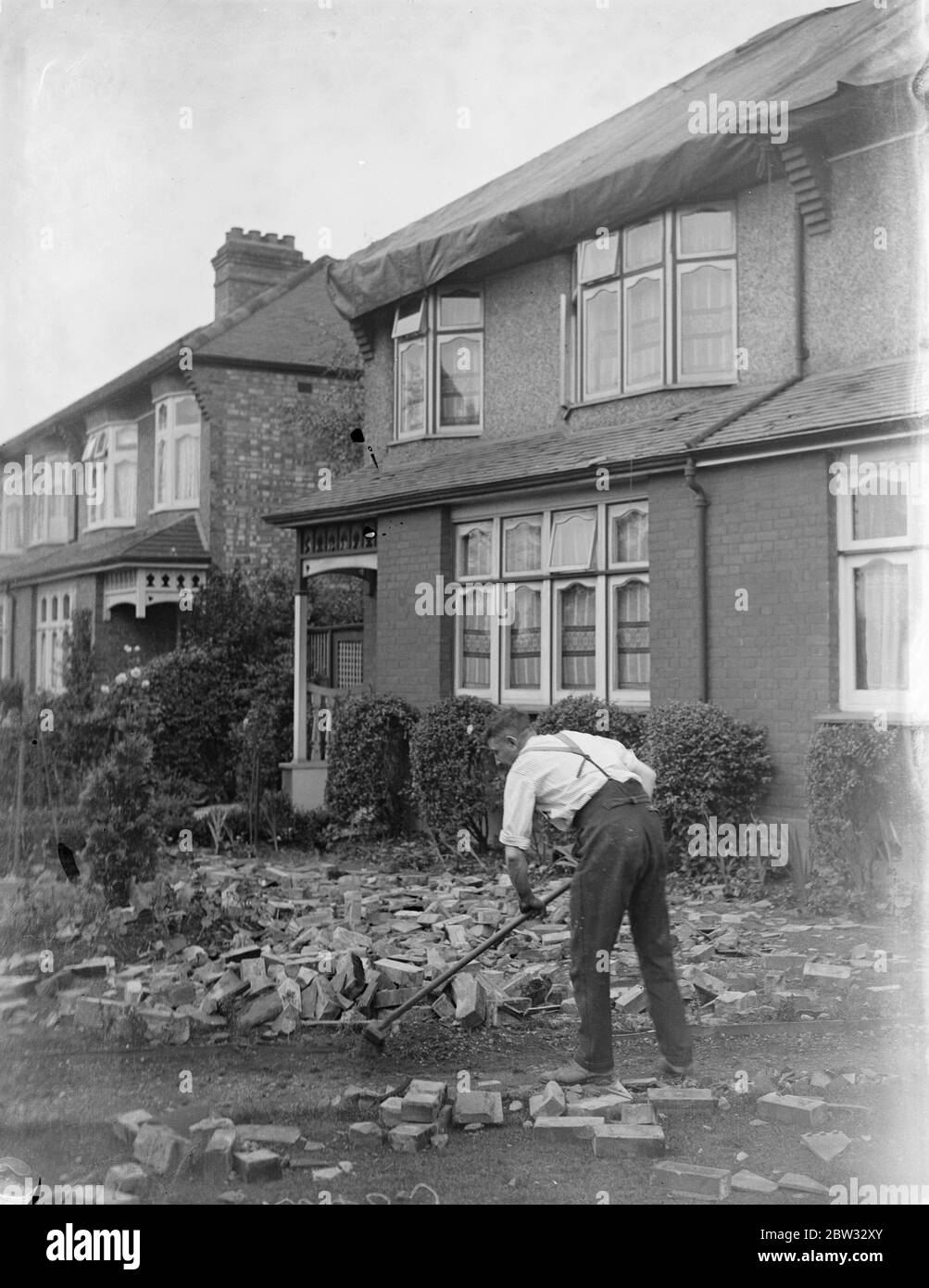 Houses damaged in great storm at Enfield . Two semi detached houses were struck and badly damaged by a thunderbolt during the great storm which broke over London . The greater part of the roof was torn away and pieces of furniture were scattered about and thrown on to the floor . Fireplaces were blown and water pipes burst . Mr Franck Higham with his wife and child were at tea when the thunderbolt came down the chimney , and had a narrow escape . Mr Frank Higham clearing away the debris from his garden after the havoc wrought by the storm . 23 July 1932 Stock Photo