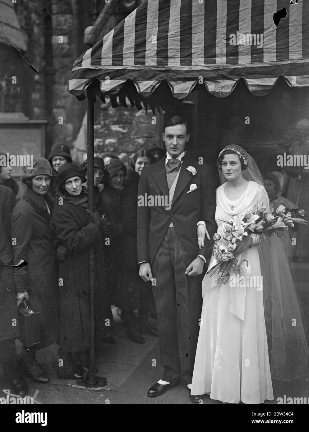 Old fashioned posing for society wedding . The bridesmaids all carried old fashioned posies and the smallest bridesmaids wore a bonnet and cape at the wedding of Miss Prudence Maxwell Lyte to Mr John Newman McClean which took place at St Peter ' s church , Cranley Gardens , London . The bride and groom leaving the church after the ceremony . 19 April 1932 . Stock Photo