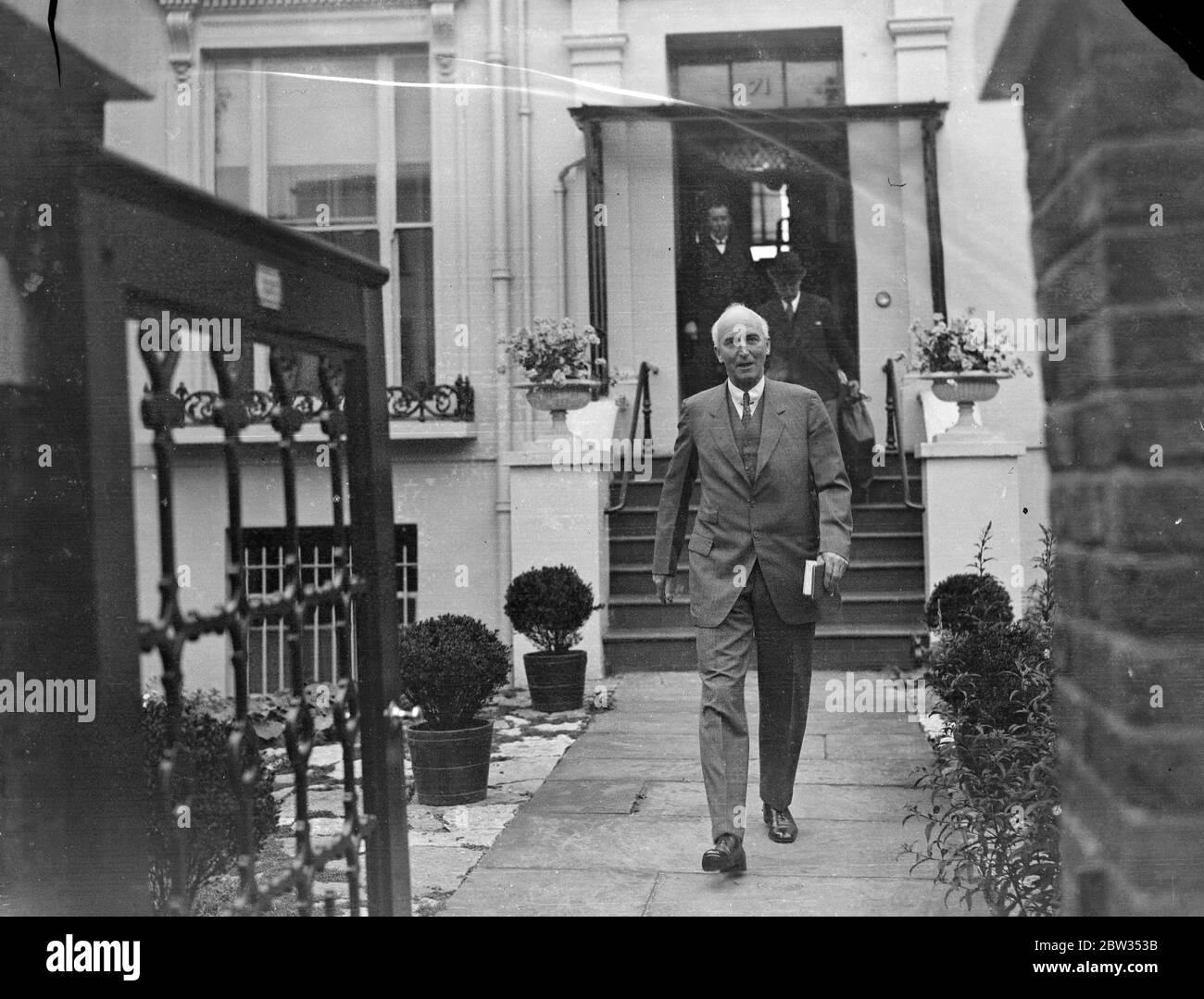 Sir John Simon leaves again for Geneva . After a hurried visit to consult members of the cabinet on the American Disarmament proposals , Sir John Simon , left London for Geneva again . Sir John Simon leaving his London home for Geneva . 28 June 1932 Stock Photo
