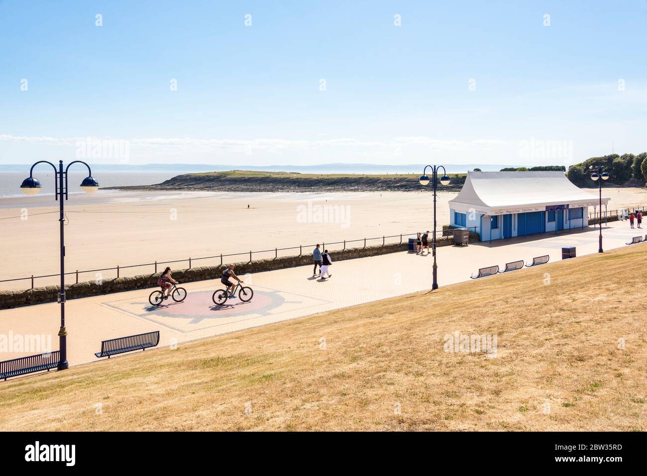 A few people walk and cycle along the promenade by the quiet beach at Barry Island on a sunny Spring Bank holiday afternoon during the 2020 coronaviru Stock Photo