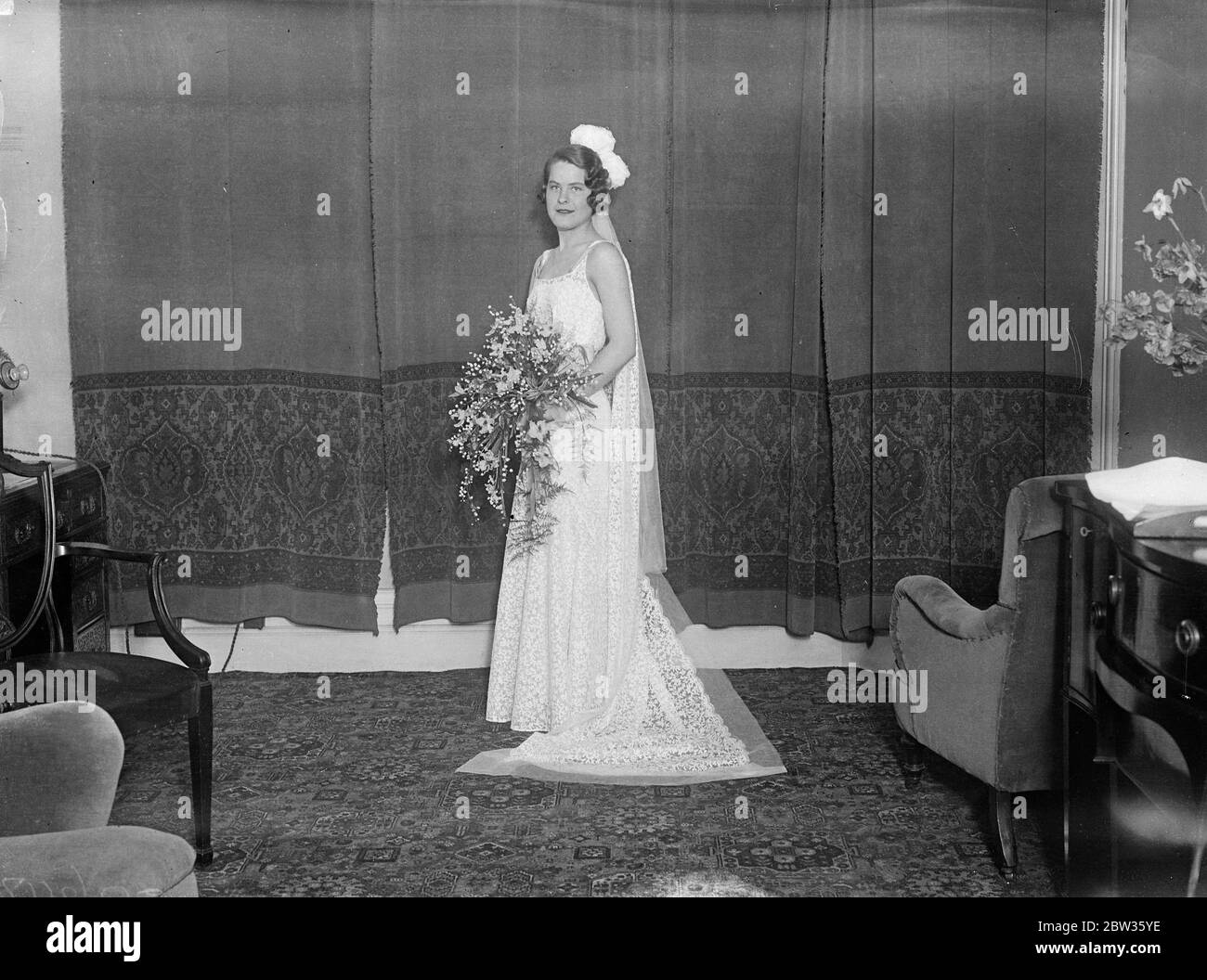 American girl to be presented at court . Miss Hannah Locke of Philadelphia , the daughter of Mrs Robert W Locke , who is among the American girls to be presented at Court by Mrs Ray Atherton , wife of the American Charge d ' Affaires . She is photographed in her gown before leaving to attend the first Court presentation at which she made her bow to the Queen , The King was unable to be present on account of rheumatism . Miss Locke ' s gown was of white lace trimmed with a dull blue taffeta belt and shoulder straps , worn with a train of white lace . Her bouquet was of white orchids and lilies Stock Photo