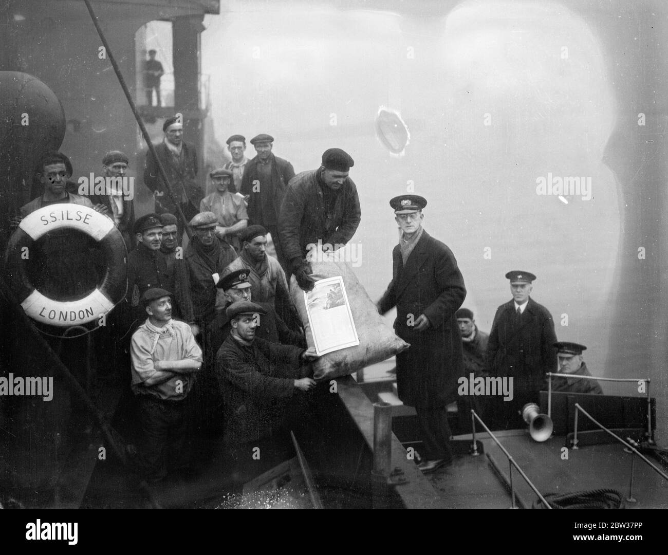Distribution of christmas gifts to Thames Watermen . The annual distribution of Christmas gifts to Thames Watermen by the missions to seaman took place on the river when Reverend F J Cutts distributed gifts . Photo shows ; The Reverend F H Cutts distributing gifts to a Sunderland collier on the Thames near Woolwich . 21 December 1933 Stock Photo