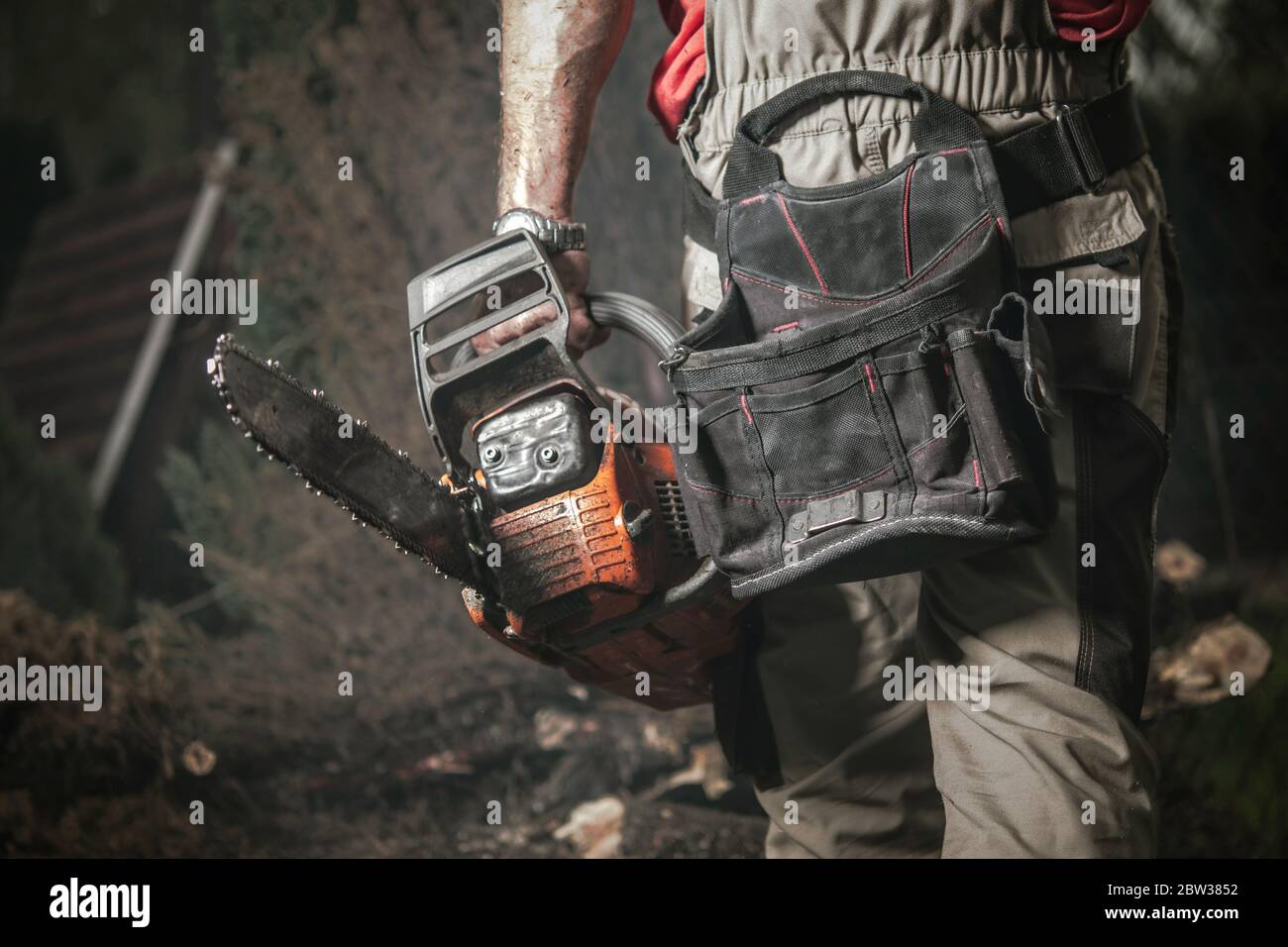 Garden Chainsaw Mechanical Saw Job Industrial Theme. Caucasian Men with Modern Professional Gasoline Powered Chainsaw in Hand Covered by Dirt. Lower B Stock Photo