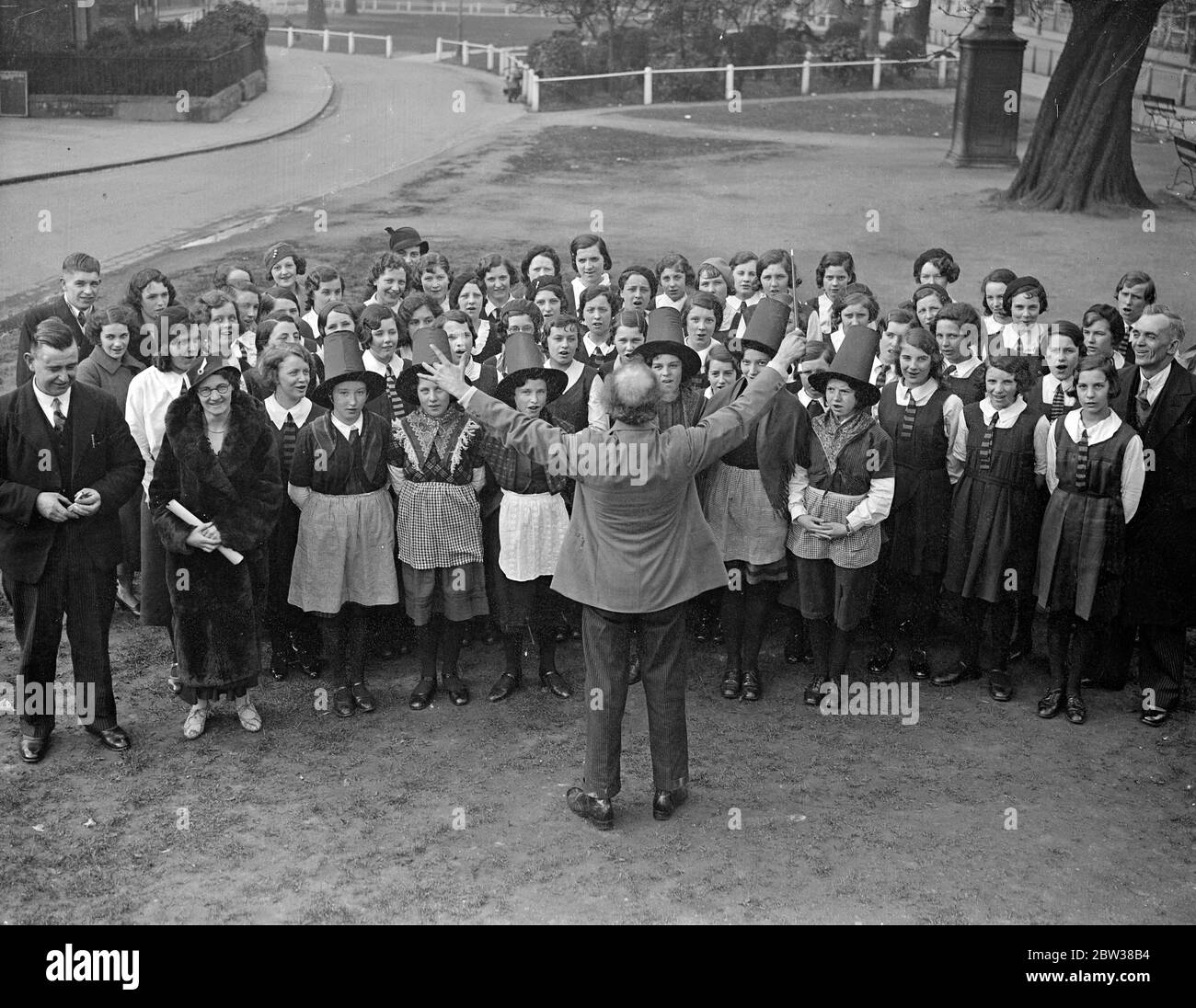 Welsh children ' s choir at Ealing in National Costume . Child members of the Aberaman juvenile choir of Wales practiced on Ealing Green before giving a concert at Ealing Town Hall . The choir has won over 300 prizes , including 11 national awards . Photo shows , the choir rehearsing on Ealing Green under the direction of their conductor , Mr Mitchelmore . 11 April 1934 Stock Photo