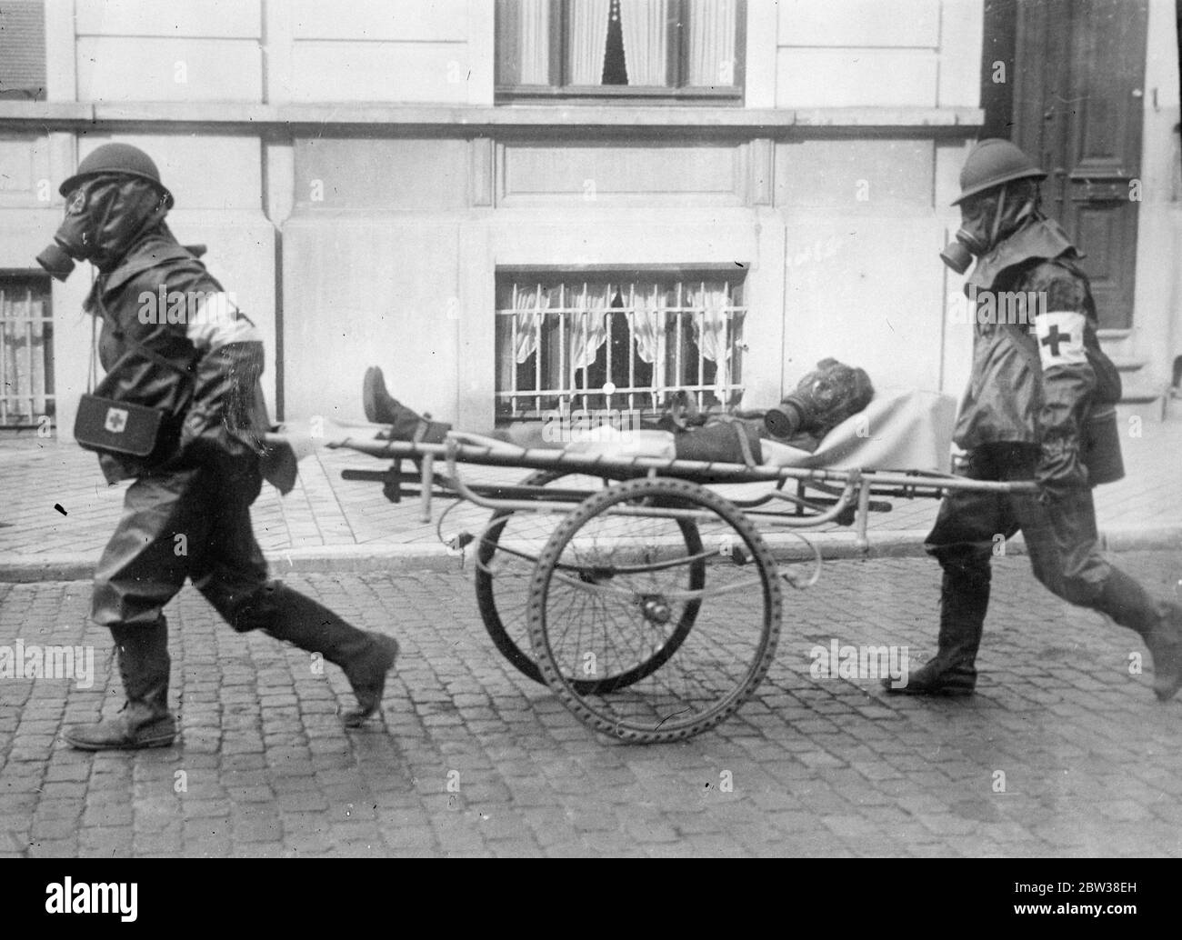 A  victim  of the brussels air raid . Gas masked ambulance men busy as bomb and gas attack is made on city . Men , women and children lay prone on the Brussels pavements when a mock aerial bomb and gas attack was made on the city to test the defences . The citizens co operated with the military authorities to make the attack as realistic as possible . Gas masked Red Cross men rushed  victims  to first aid centres , and fire fighters wearing gas masks concentrated their efforts on buildings set alight by the  bombs  . A child  victim  of the raid being rushed by gas masked Red Cross men to a fi Stock Photo