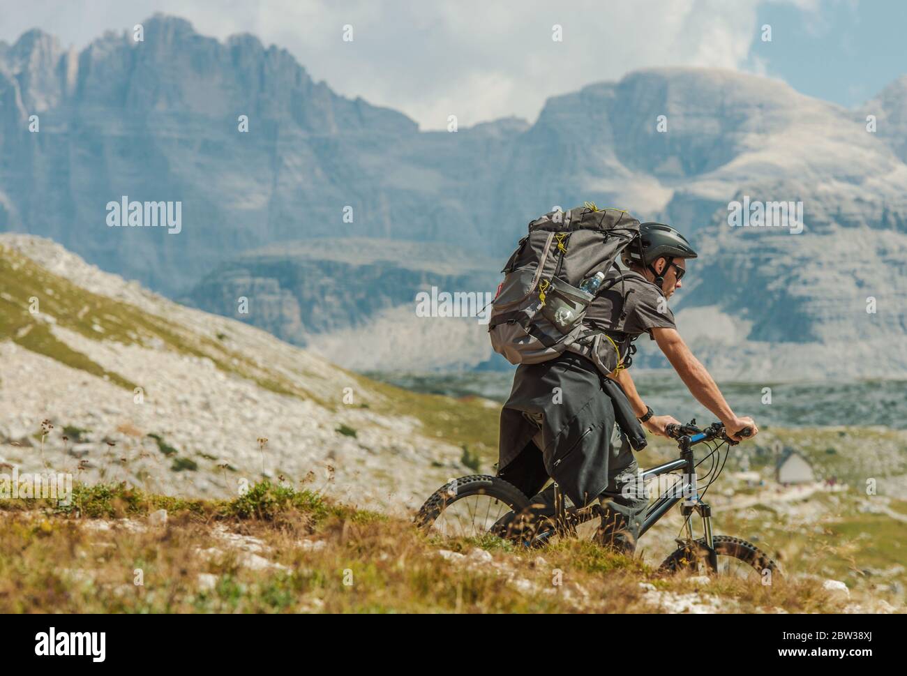 Caucasian Biker in His 30s Wearing Large Backpack Riding on the Mountain Trail in Italian Dolomites near Misurina, Italy. Outdoor Sports and Recreatio Stock Photo