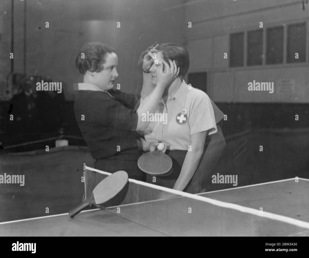 Table tennis championships at Imperial Institute , Kensington . Left is Mlle Wyes , putting some sticking plaster on Mlle Osley eye after damaging her during play . Two Swiss players . 9 February 1935 Stock Photo