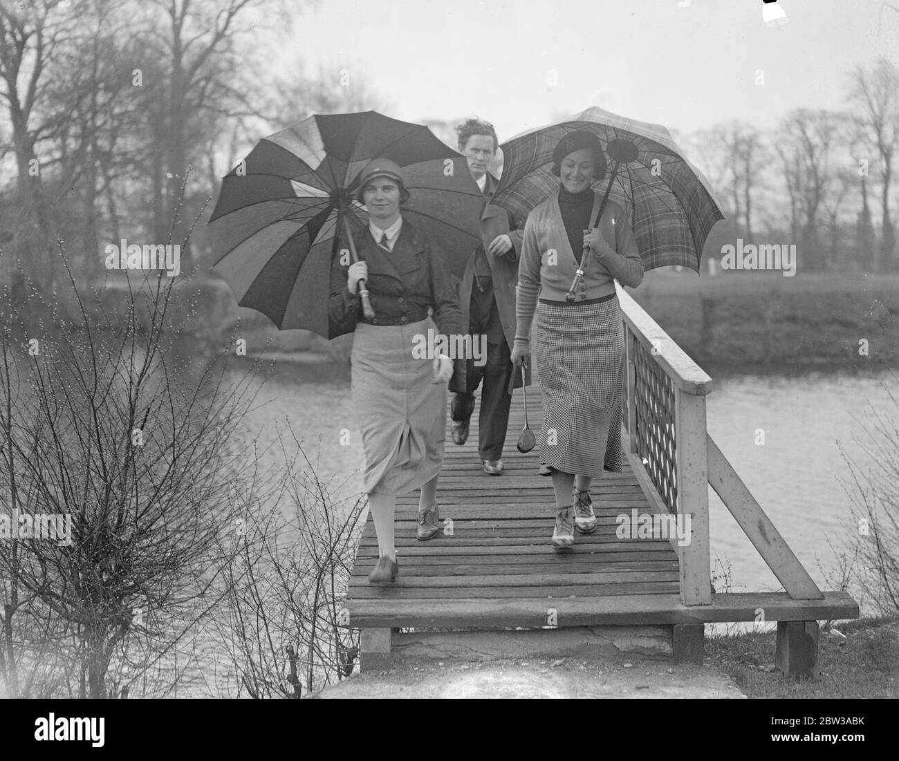 Women ' s international golf tournament opens in the rain at Ranelagh . The ladies golf union international tournament opened in the rain at the Ranelagh Club , Barnes . Photo shows Miss Eithne Penteny ( left ) and Miss B Gaysford , crossing the bridge beneath umbrellas . 11 April 1934 Stock Photo