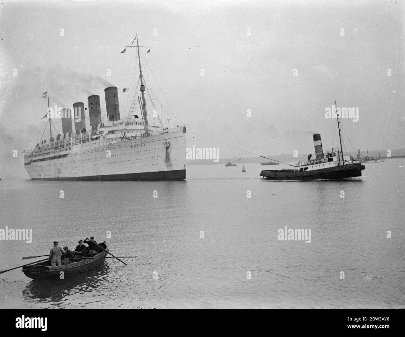 Mauretania to undergo refit not to be scrapped . Picture shows the liner being towed into harbour by a tug boat , men in rowing boat in foreground . 3 October 1934 Stock Photo