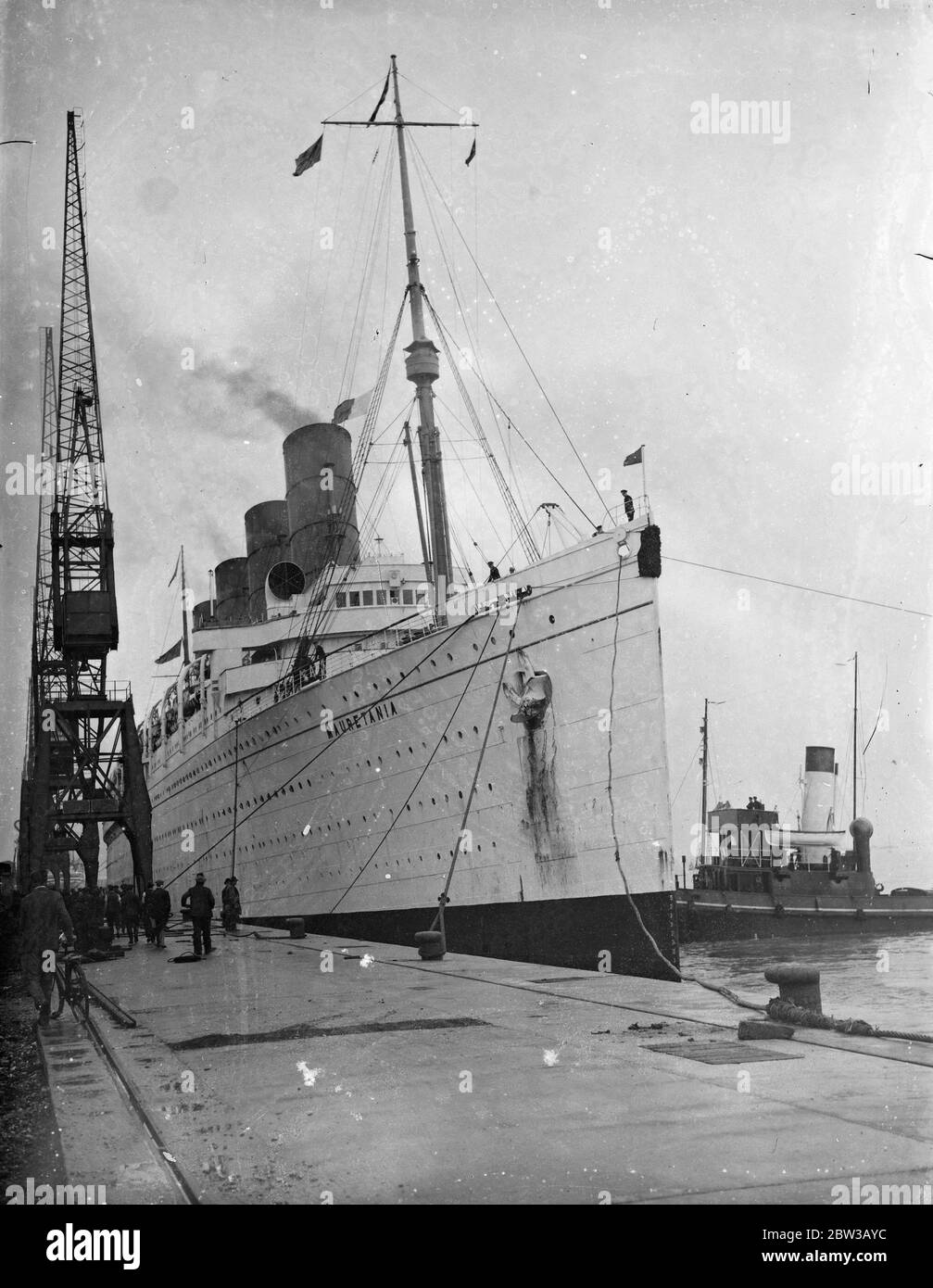 Mauretania to undergo refit not to be scrapped . Picture shows ship docked in port with tug boat alongside. 3 October 1934 Stock Photo
