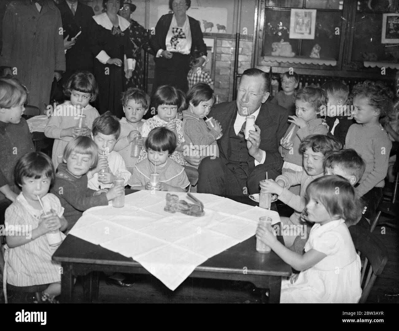 Mr Walter Elliot Minister of Agriculture drinks milk with children at a London school . 1 October 1934 Stock Photo