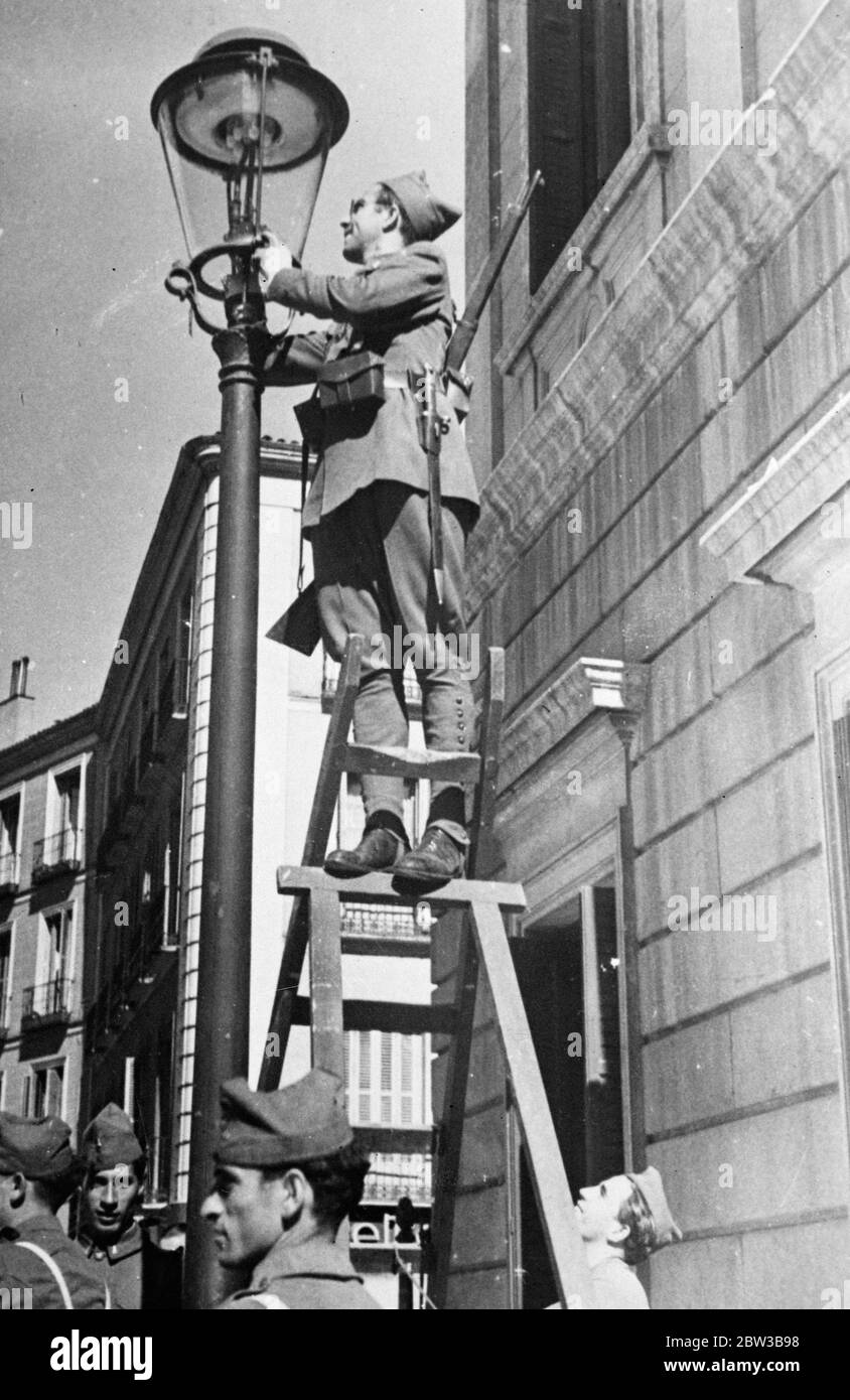 Soldier lighting a street lamp in Madrid , Spain , as his comrades mount guard . 9 October 1934 . Stock Photo
