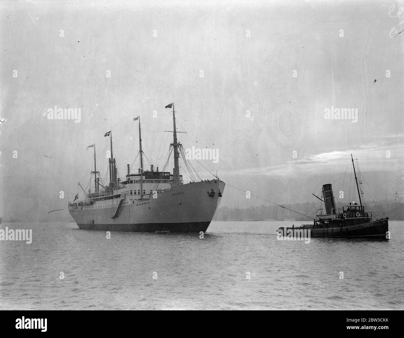 A tug pulls the Danish ship ,  Jutlandia  up the Thames to Tilbury , carrying the King and Queen of Denmark as they arrive for the for the royal wedding . 26 November 1934 Stock Photo
