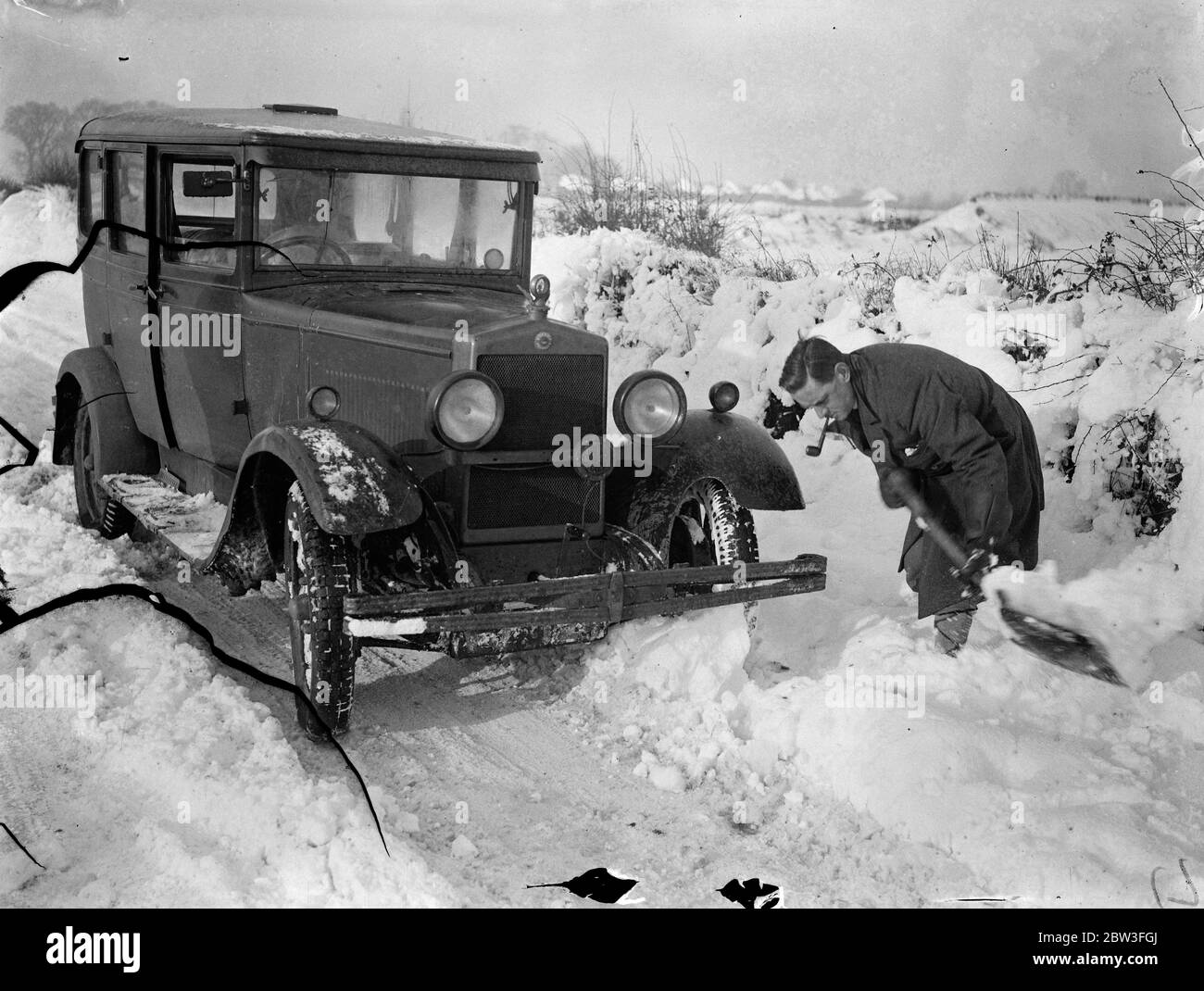 Snowdrifts hold up traffic in Hertfordshire . Photo shows ; A motorist digging a car out of a drift on the Ware , Bishops Stortford road . 27 January 1935 Stock Photo