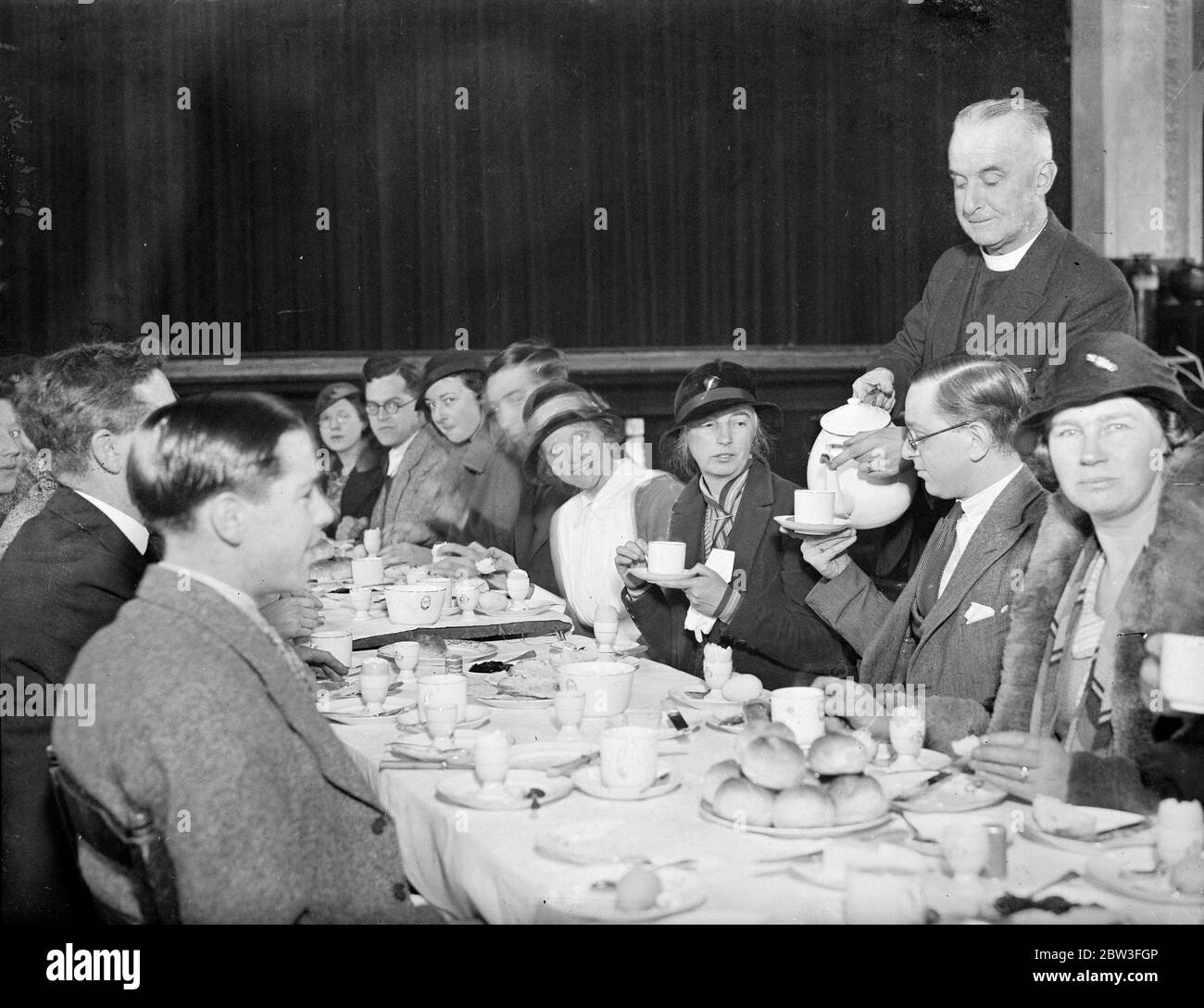 Vicar of St John ' s Church , Hampton , Wick , Middlesex , provides free breakfasts for his early morning flock . Photo shows ; The vicar ( the Reverend A Meyrick Johnson ) helping one of his parishioners to a cup of coffee at the free breakfast provided after Holy Communion . . 27 January 1935 Stock Photo