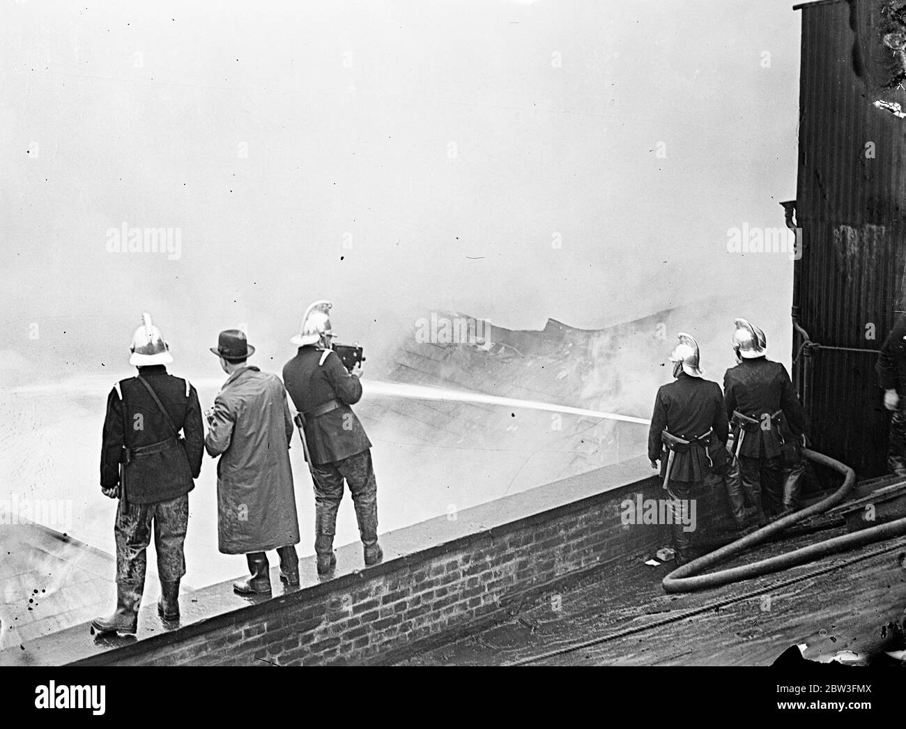 Firemen film London rice factory ablaze . Firemen made a moving picture recording of the great blaze at St George ' s Wharf a rice warehouse of Carbutt and Comapny , ltd in Shad Thames , Bermondsey . About 250 firemen fought the flames . Photo shows , firemen filming the blaze . 1 April 1936 Stock Photo