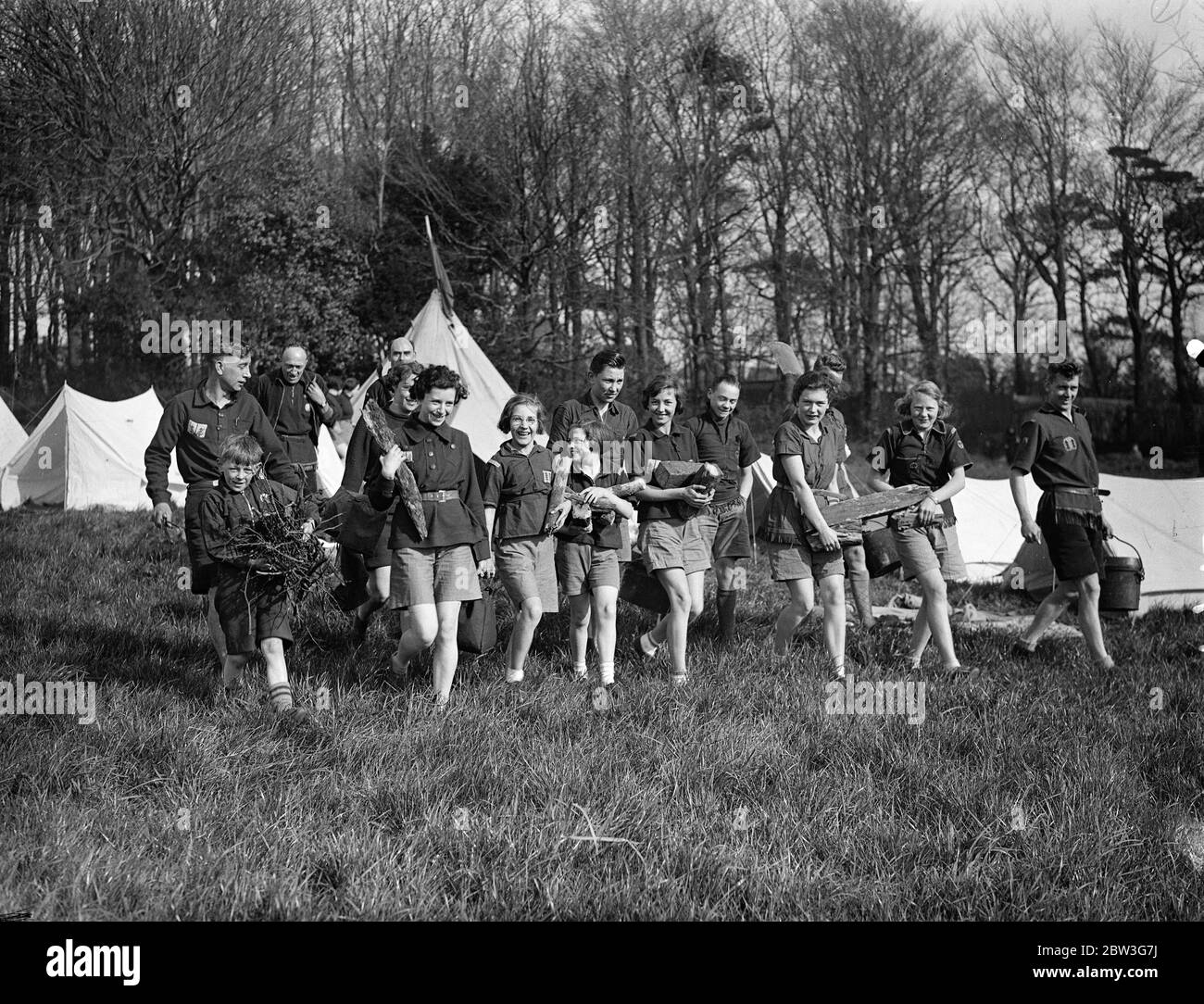 Best task of the day . Order of woodcraft chivalry members in Sussex , Easter Camp . Wearing the quaint and picturesque costumes of their organisation , members of the Order of Woodcraft Chivalry , the outdoor association formed for youths and girls , have gone into camp near Brighton for Easter holiday . Members of the Order are of all ages and come from every county in England to the Sussex camp . Photo shows ,the young fatigue party bringing in food and wood for the camp cookhouse . 11 April 1936 Stock Photo