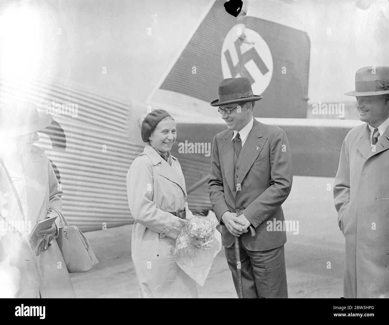 Nazi perfect woman arrives by air to attend London conference . Frau Gartrud Scholz Klink , Germany ' s perfect Nazi women , arrived at Croydon Aerodrome by air , to attend the Third International Congress for Social Work in London . Frau Scholz Klink , who is not yet 40 is here of the National Socialist womanhood . She fulfills all the idols of Nazi womanhood , and is an ardent advocate of the ' back to the kitchean movement . She was welcomed by Prince von Bismarck , German Charge d ' Affaires in London . Photo shows , Frau Gatrud Scholz Klink chatting with Prince von Bismark on arrival at C Stock Photo