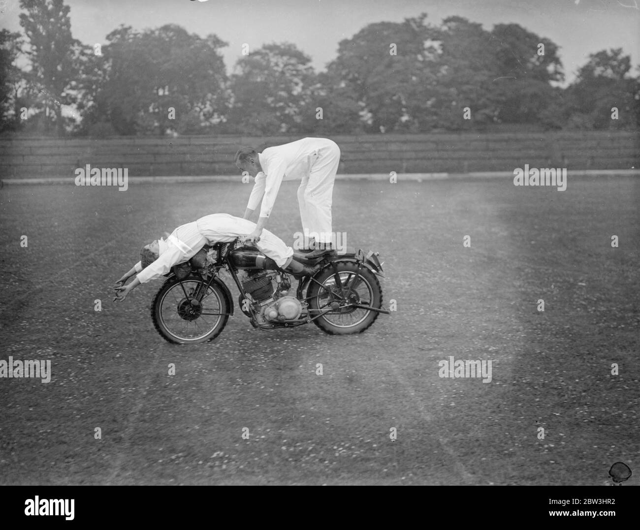 They keep their balance ! . Jessie Hole , whose idea of home is two wheels separated by a motor engine , lies at ease over the the handle bars , as her brother , George Hole , tries some acrobatic moto cycle riding at the Crystal Palace , London . 12 July 1936 Stock Photo