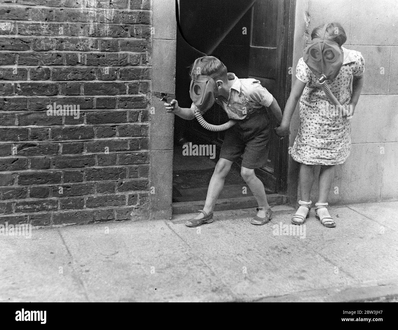 Modern children fight their battles in gas masks . Toy soldiers and cannos are not sufficient for the mimic warfare of modern childen , They are bringing ideas up to date and fighting their battles in gas masks . Two London children stalking the enemy in gas masks . 30 July 1935 Stock Photo