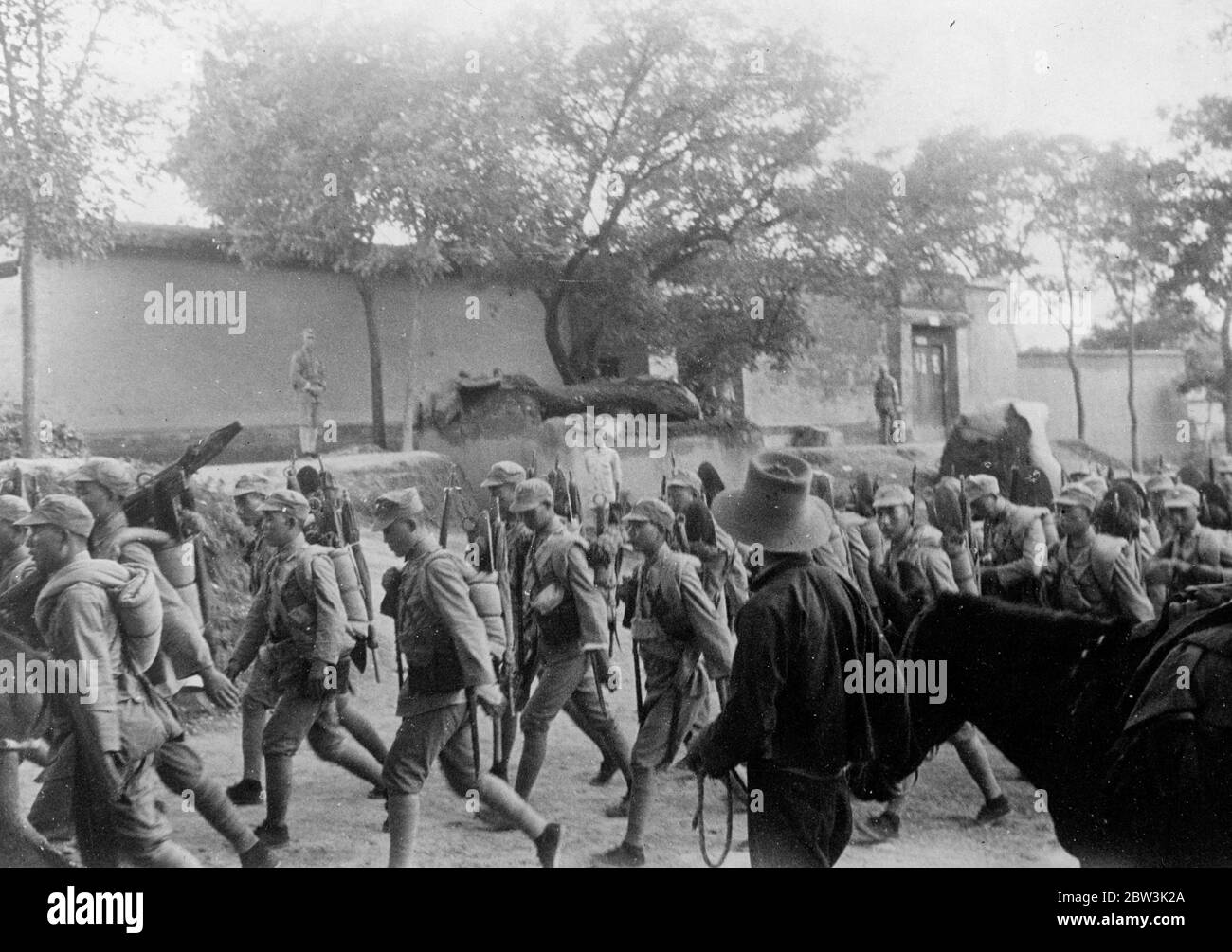 Chinese troops march to defend capital . This picture , just received in London , shows Chinese troops rifles and blankets slung across their shoulders marching through a village to the north o Shanghai , on their way to help in the defence of Nanking , the capital which is now threatened by the Japanese . These troops were forced to retreat from Shanghai and hurriednorth to reinfore Nanking ' s defenders . 21 November 1937 Stock Photo