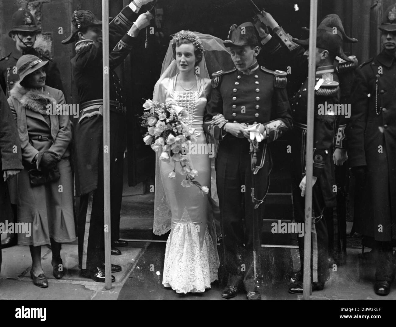 Naval Guard of Honour at Mayfair wedding . The wedding of Lieutenant the Hon David Cairns , RN , to Miss Barbara Harrison Burgess took place at Christ Church Down Street , Mayfair . The bridegroom is a brother of Lady Katherine Cairns . Photo shows , the bride and groom passing through the guard of honour outside the church after the ceremony . 16 April 1936 Stock Photo