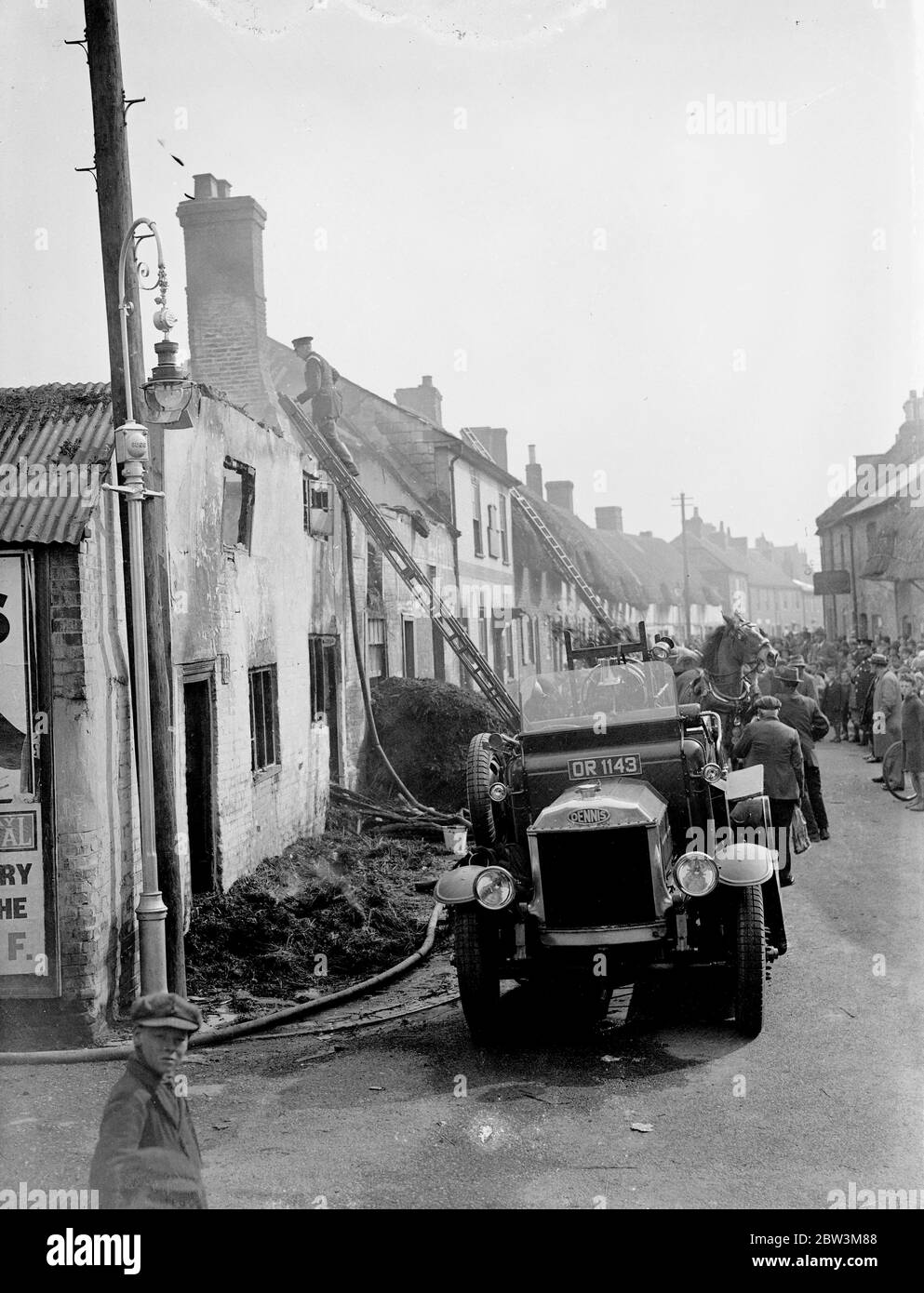 Four thatched cottages ablaze in big fire in Andover . Four thatches cottages blazed furiously in one of the worst fires seen in Andover ( Hampshire ) for 35 years . Whilst scores of helpers tried to save the furniture of the doomed cottages , firemen strove to prevent the flames spreading to many other thatched cottages nearby . Eighteen people are homeless as a result of the blaze , mr and mrs Bacon , one of the families who have lost their home have six children . Photo shows , firemen at work on the blaze . 8 May 1936 Stock Photo