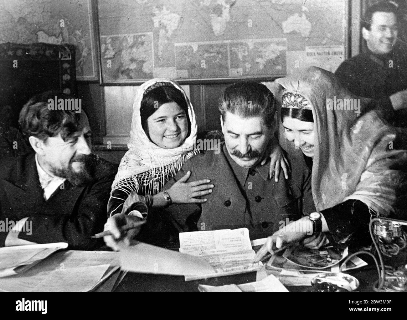 Arms around Stalin , a dictator softens . This is one of the most human photographs of a dictator ever made . Joseph Stalin , Soviet Russia ' s ' Man of Iron ' , is seen responding to the advances of 11 year old Mamlakat Nakhangove ( left ) and Ene Geliyeva ( right ) , members of a party of collective farmers from Tajikistan in Soviet central Asia , , who conferred with Stalin in Moscow . In this picture Stalin is autographing photographs at the conference . Extreme left is M A Chernov . People ' s Commissar for Agriculture . 11 December 1935 Stock Photo