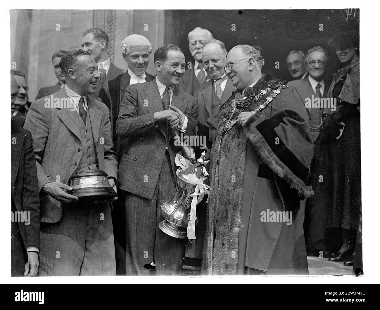 Arsenal team given civic reception at Islington . Drive through crowded streets . The Arsenal team , English Cup winners , carrying the F A Cup , drove through large crowds to the Islington Town Hall , where they were given a civic reception . The team was received by the Mayor , Councillor H G Coleman , himself an old footballer , at the town hall . Photo shows , Alex James , the Arsenal captain , being received by the Mayor of Islington , Councillor H G Coleman , at the Town Hall . 28 April 1936 Stock Photo