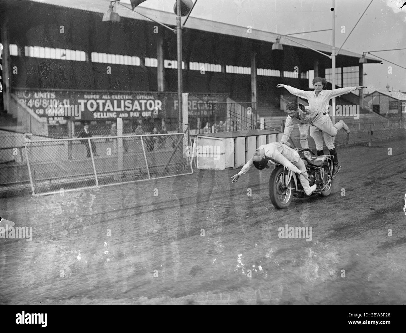 These girls like a change from pillion riding . A breath taking display of acrobatic motor cycle riding was given at Hackney Wick Stadium , London , by Putt Mossman and members of his team of speedway riders . Aiding Mossman in his stunts are his wife , Mrs , Helen Mossman , and his sister , Miss Dessie Grant . Mossman ' s is the first American speedway team to visit England and they are to have matches with British teams . Photo shows , Putt Mossman takes his wife and sister for a peculier sort of joy ride . Reclining on the handle bars is Mrs Helen Mossman . Standing behind is Mossman ' s si Stock Photo