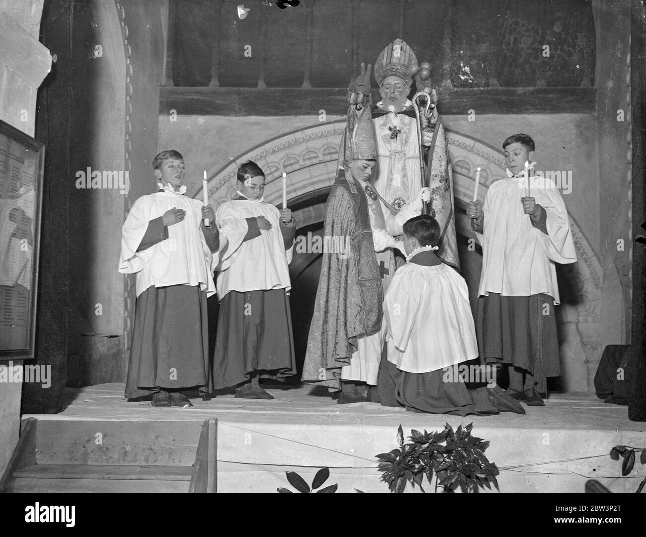 Boy Bishop enthroned in the first public ceremony since the reformation at Guilford . Fred Brazier , aged 12 chosen as ' Boy Bishop ' of St Mary of the Angels song school , Highgate , was enthroned by the Rev Desmond Morse Boycott as St Nicholas , at Compton church , Guilford , Surrey , in the first public ceremony since the reformation . Photo shows , the Chaplain kissing the boy bishop as St Nicholas blessed them during the ceremony . 6 December 1935 Stock Photo