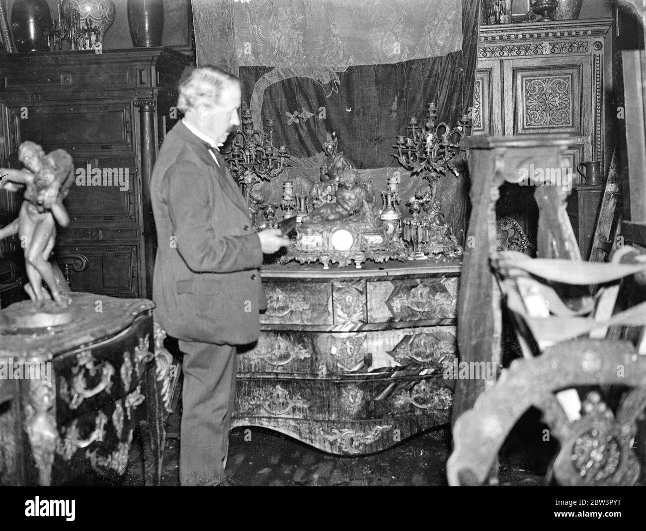 Art treasures and antiques ruined in Hampstead fire , Willoughby Road . Mr Ernest Stamp inspecting some of his damaged antiques , including a Louis XIV commode . 7 August 1935 Stock Photo