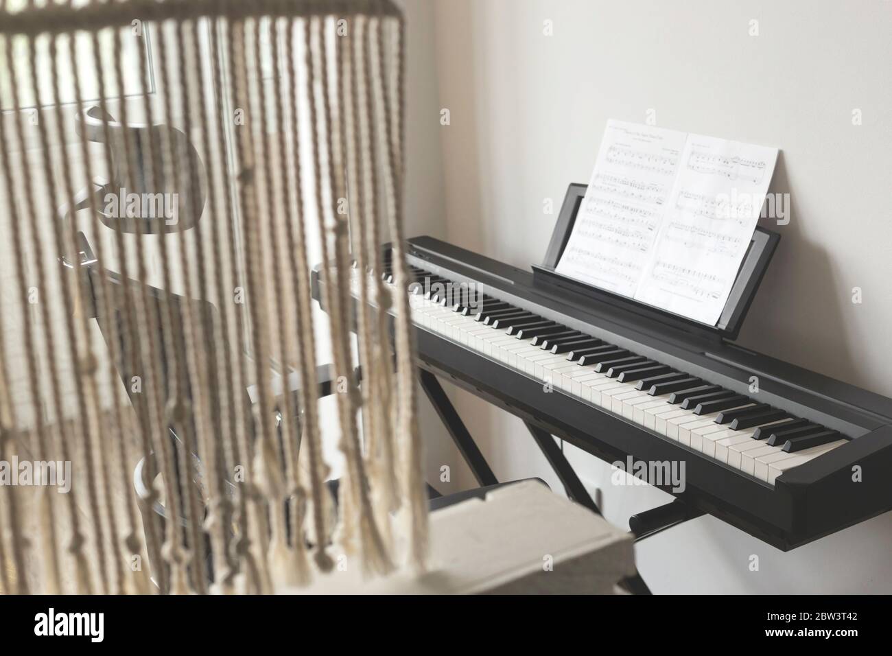 Electronic piano with notes in a light cozy interior. Hobby at home concept. Stock Photo