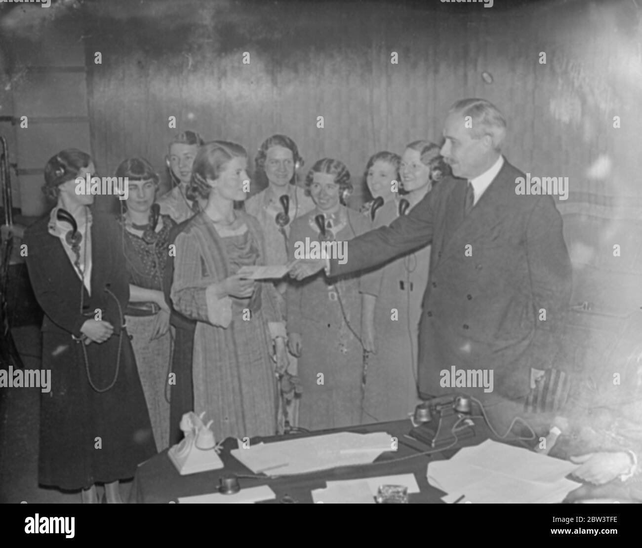 London telephone girl wins golden voice competition . M/S of Miss E. W. Cain sat at a switchboard reading poetry into the mouthpiece, other operators sit behind her. M/S of Postmaster General Major Tryon thanking the judges. M/S as the camera pans across the judges who are, Stuart Hibberd of the BBC (British Broadcasting Company / Corporation), Dame Sybil Thorndike, John Masefield, the Poet Laureate, Mrs Atkinson, chosen as the perfect telephone subscriber, and Lord Iliffe, they are all listening to Miss Cain speak through the telephone. Hibberd asks Sybil what she thinks of her voice and she Stock Photo