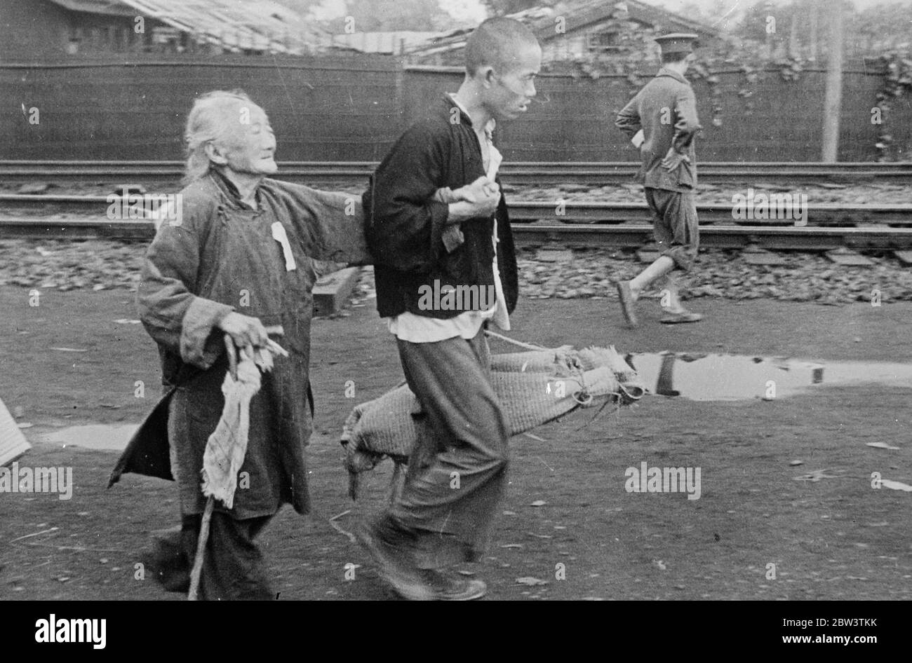 War has no pity for aged ! . An aged Chinese woman , one feeble hand clasping her stick , desperately endeavours to keep her flagging body abreast with her companion as they fly from the Shanghai war zone . The man carries the old woman ' s few possessions in a small bundle . 21 November 1937 Stock Photo