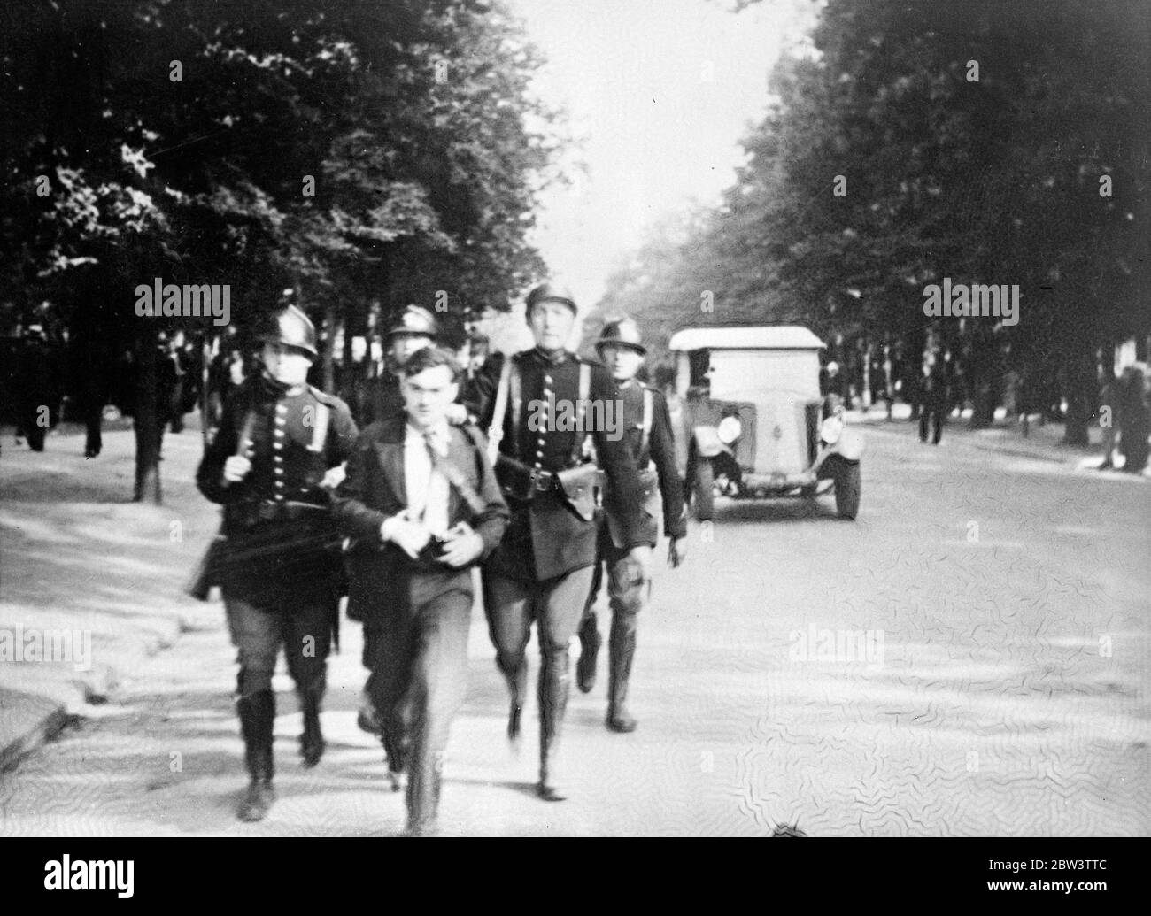 Brest rioters tear up paving stones as missles against police and troops . RIosters in Brest shipping strike caused through the French Goverment ' s econmy cuts . Photo shows , mobile guards escorting an arrested rioter after a serious clash in Brest . 8 August 1935 Stock Photo