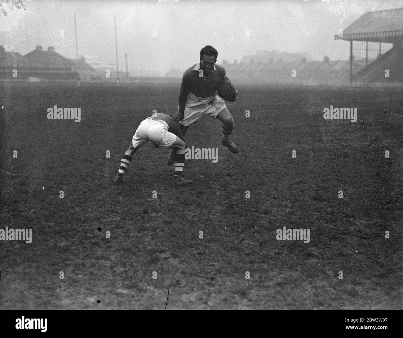 George Nepia , famous all black , has trial before debut in London league rugby . George Nepia , considered the greatest rugby full back since the war , had a trial at Mitchs Stadium , having arrived in London to play rugby league football for the Streatham and Mitcham Club . Nepia casued a sensation in 1924 when he was a star member of that famous all black side . Nepia has hopes of playing tomorow ( Saturday ) against Wigan , but the decidion depends on the result of his tryout today . Photo shows , George Nepia handing off an opponenet during the trial at Mitcham . 13 December 1935 Stock Photo