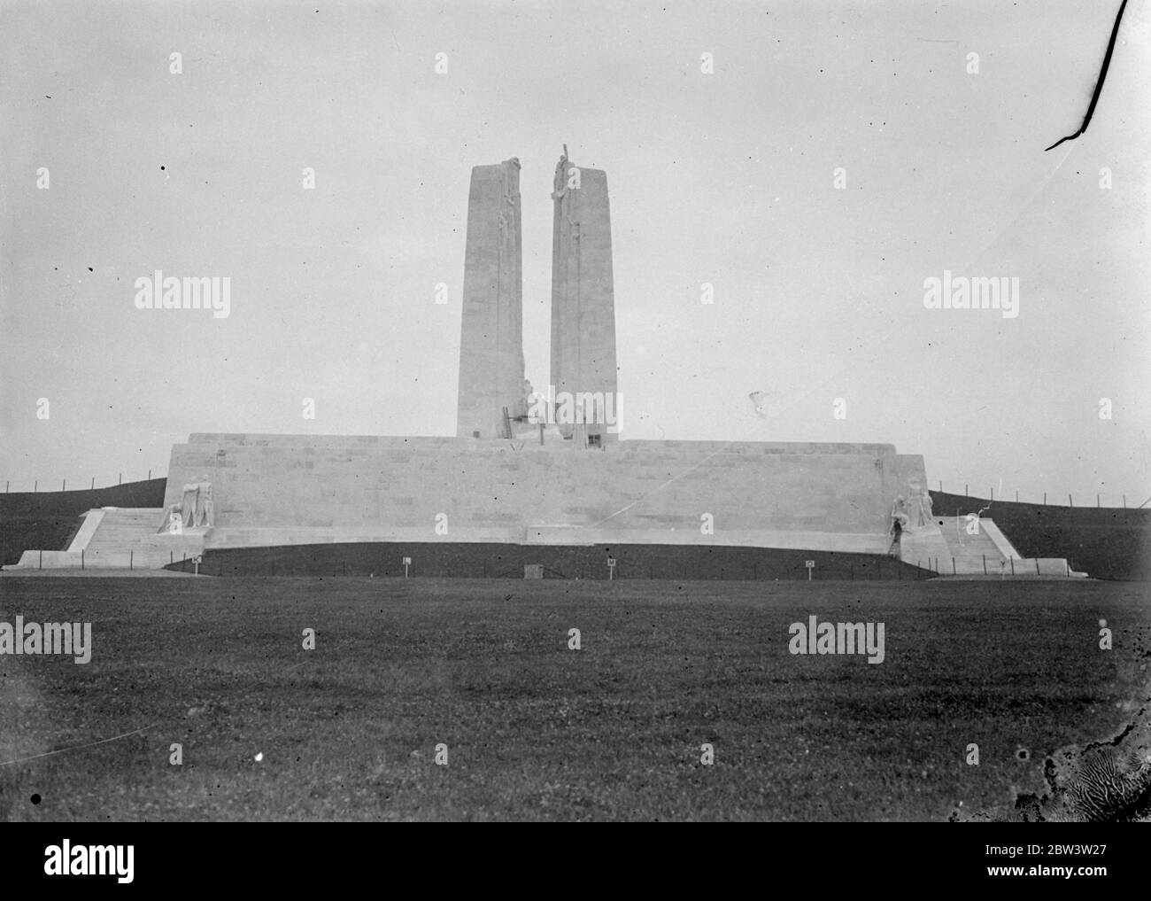 Peace-the need for a memorial of war. In the call of the summer afternoon, the placid sheep graze leisurely in the shadows of the impessive memorial erected to the memory of the 11,700 men of the Canadian forces who fell on the fields where only their bleating now disturbs the peace once racked and tortured by the heavy guns of war . The 138 feet shrine towers of the surrounding area . The work of Mr Walter Allward , the Canadian sculptor , the 30 , 000 ton memorial stands on 240 acres of ground presented to Canada by the French Government . Twin grey rear to the sky, the Vimy Ridge Memorial i Stock Photo