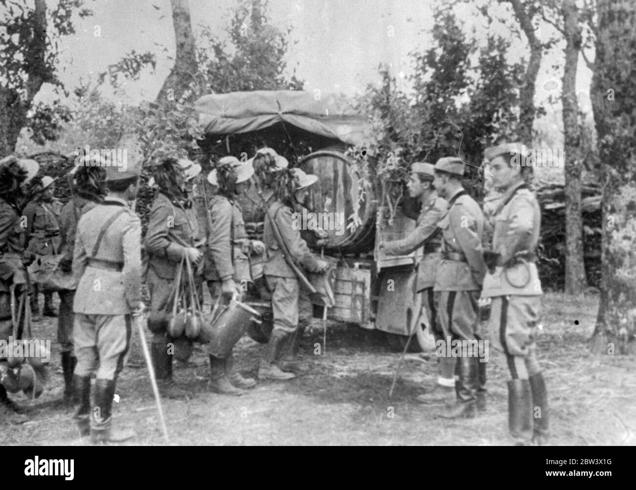The Italian Must Have His Wine - Even In  War  ! Army wagons bearing huge casks are a welcome sight to thirsty Italian soldiers taking part in the manoeuvres in Irpinia . They know that the wine issue is not far off ! Photo shows : Italian soldiers with camouflaged helmets receiving their wine issue on manoeuvres . 26 August 1936 Original caption from negative Stock Photo