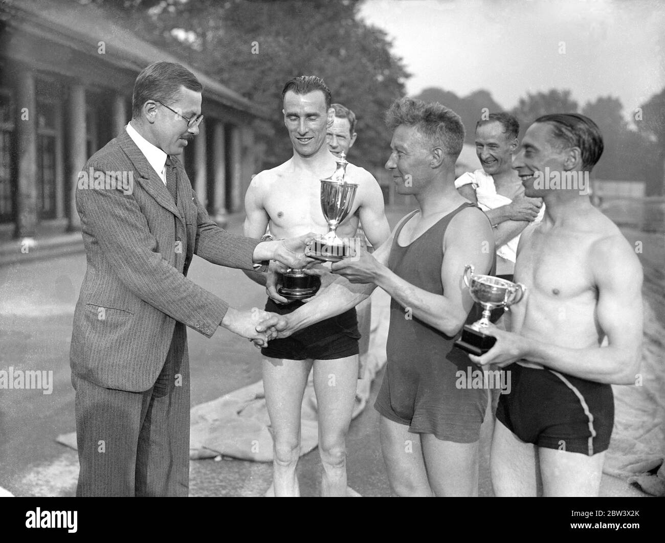 W A Lacey won the swimming race for the Varley Trophy in the Serpentine , Hyde Park . B C Wheeler was second and S Levy was third . The trophy was handed to the winner by Dr J F Varley , son of the donar . Photo shows , Mr J F Varley presenting the trophy to Lacey , left to right , Dr Varley R C , Wheeler ( second ) , W A Lacey and S Levy ( third ) . 27 August 1936 . Original caption from negative Stock Photo