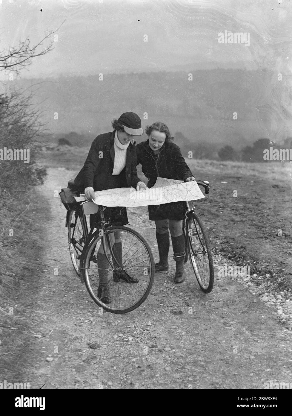 Photo shows: girl cyclists reading maps. Girls who spent their holiday a-wheel admiring the magnificent view at Newlands Corner, the famous Surrey beauty spot between Dorking and Guildford. 28 March 1937 Stock Photo