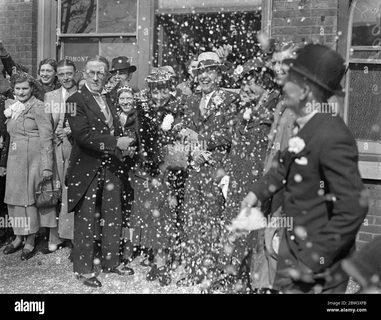 60 weddings were performed at White Hart Lane Register Office, Tottenham, today. This is the peak day for Easter holiday rush where 30 ceremonies will be performed. Photo shows-Mr Walter Grimaldi, the registrar, congratulating couples under a shower of confetti. In 25 years Mr Grimaldi has performed 20,000 weddings, believed to be a record for the country. 27th March 1937 Stock Photo