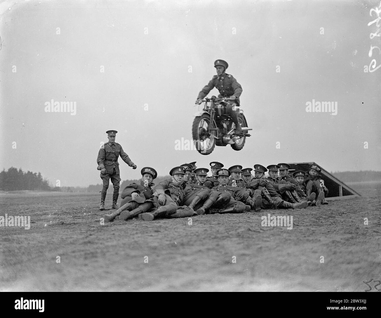 The London Divisional Signals (City of London Signals), Territorials, rehearse the display of trick motorcycle riding at Mons Barracks, Aldershot, in preparation for the Royal Tournament, which opens at Olympia on May 27. Photo shows one of the trick riders flying over his comrades who are sitting on the ground 27th March 1937 Stock Photo