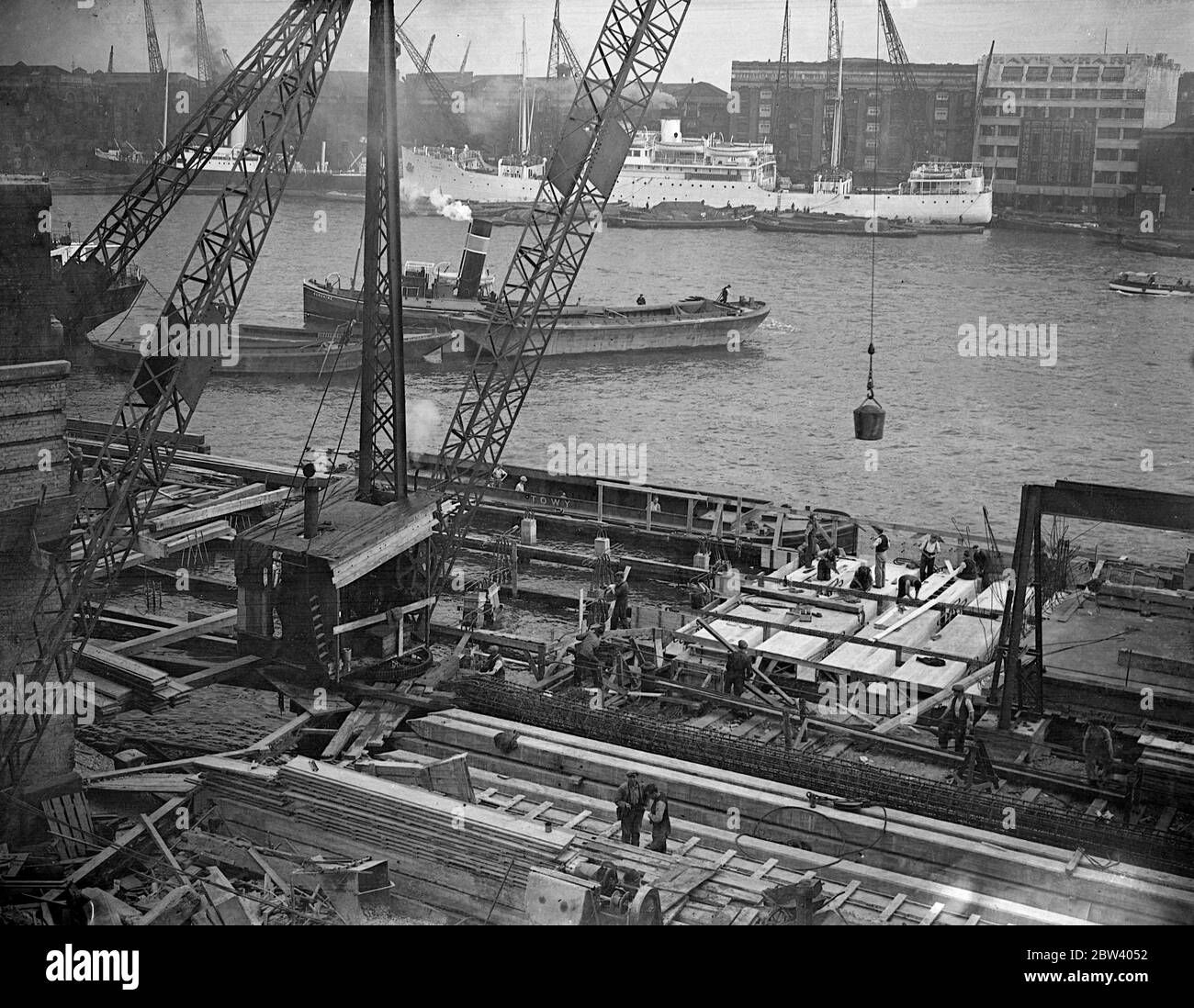 Demolition and construction at London Bridge . Demolition and construction work being carried on side-by-side in the shadow of London Bridge . The wharfage of the pool of London is being extended by an addition to Fresh Wharf and an old warehouse is being demolished to make way for a great new building . Photo shows, extending the wharfage Fresh Wharf , lower Thames Street , London Bridge . 19 September 1936 Stock Photo